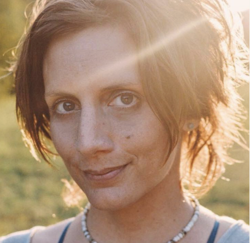 A woman with short brown hair and light skin smiling outdoors in sunlight.