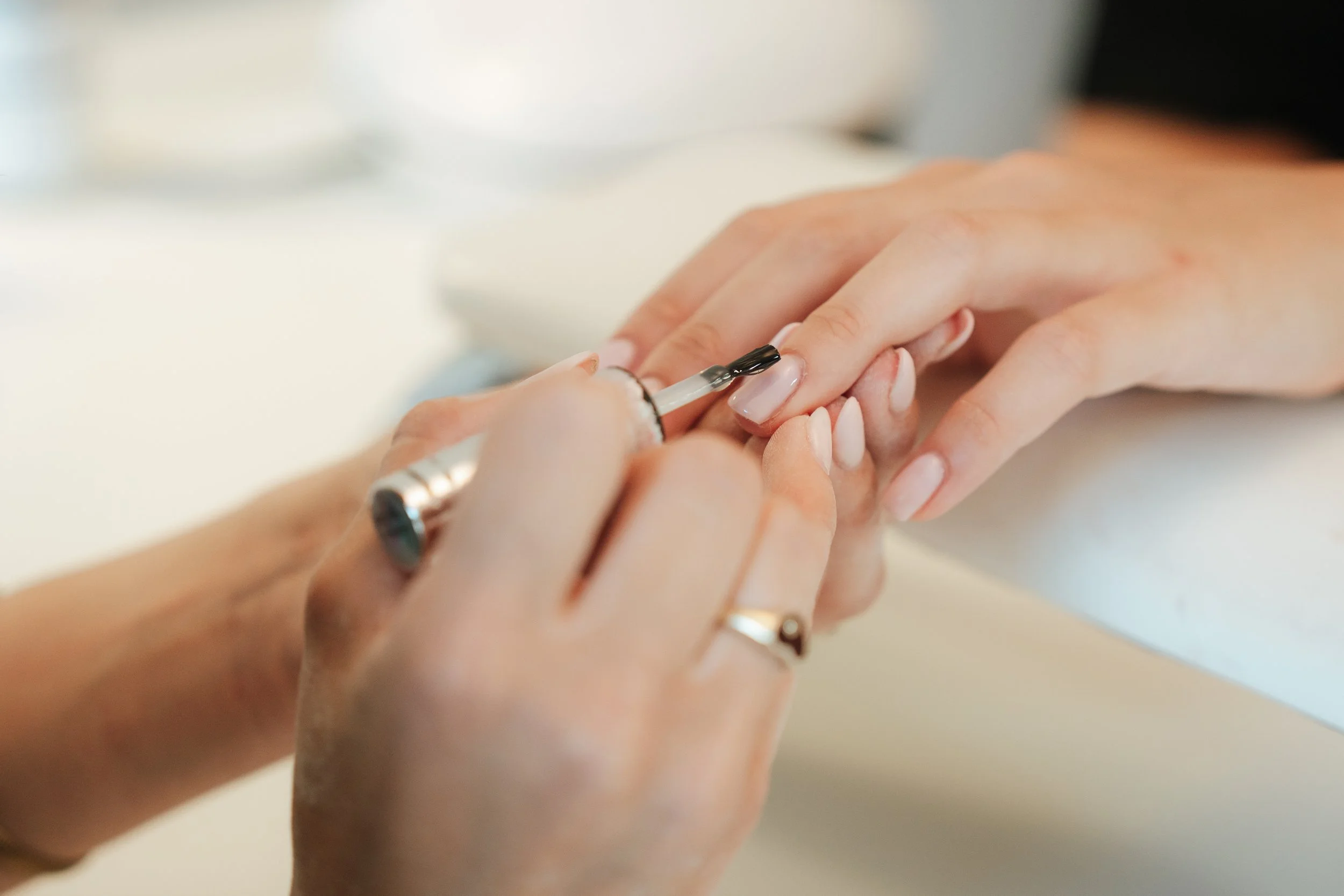 Close-up of a person's hand getting a manicure, with someone applying clear nail polish.