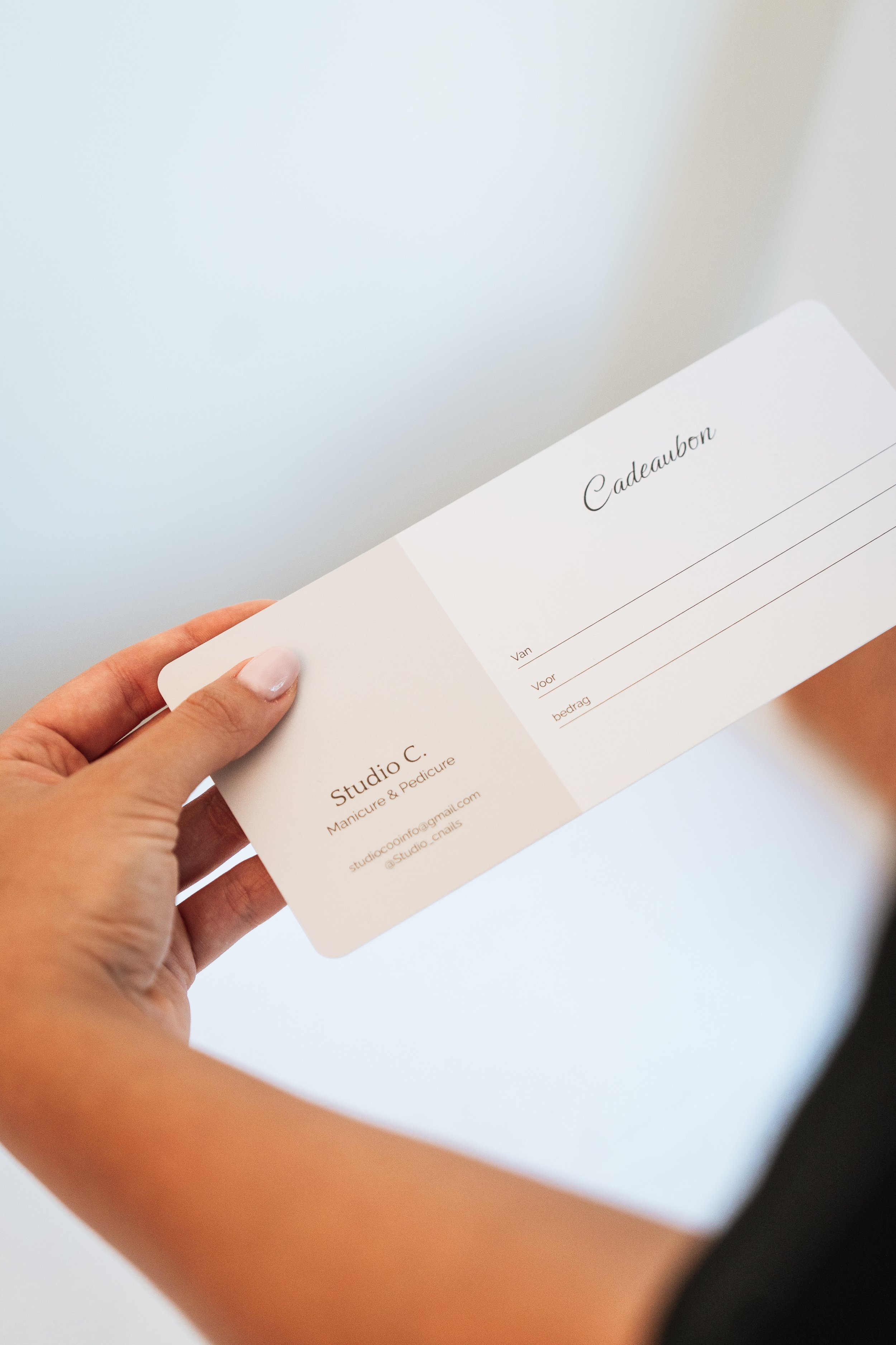 A hand holding a gift certificate with the word 'Cadeaubon' written on it, against a plain background.