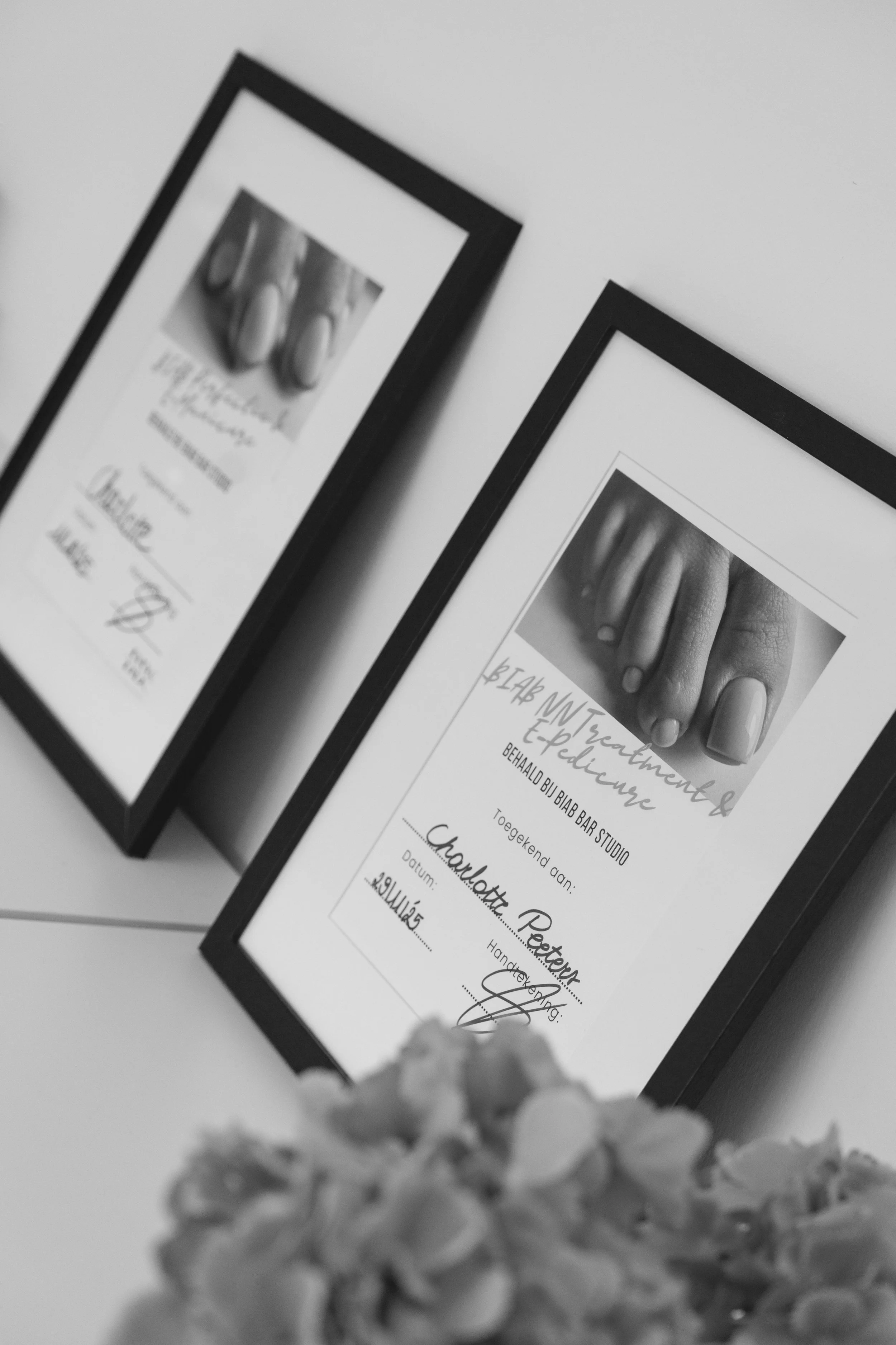 Black and white photo of framed certificates on a wall, with a bouquet of flowers in the foreground.