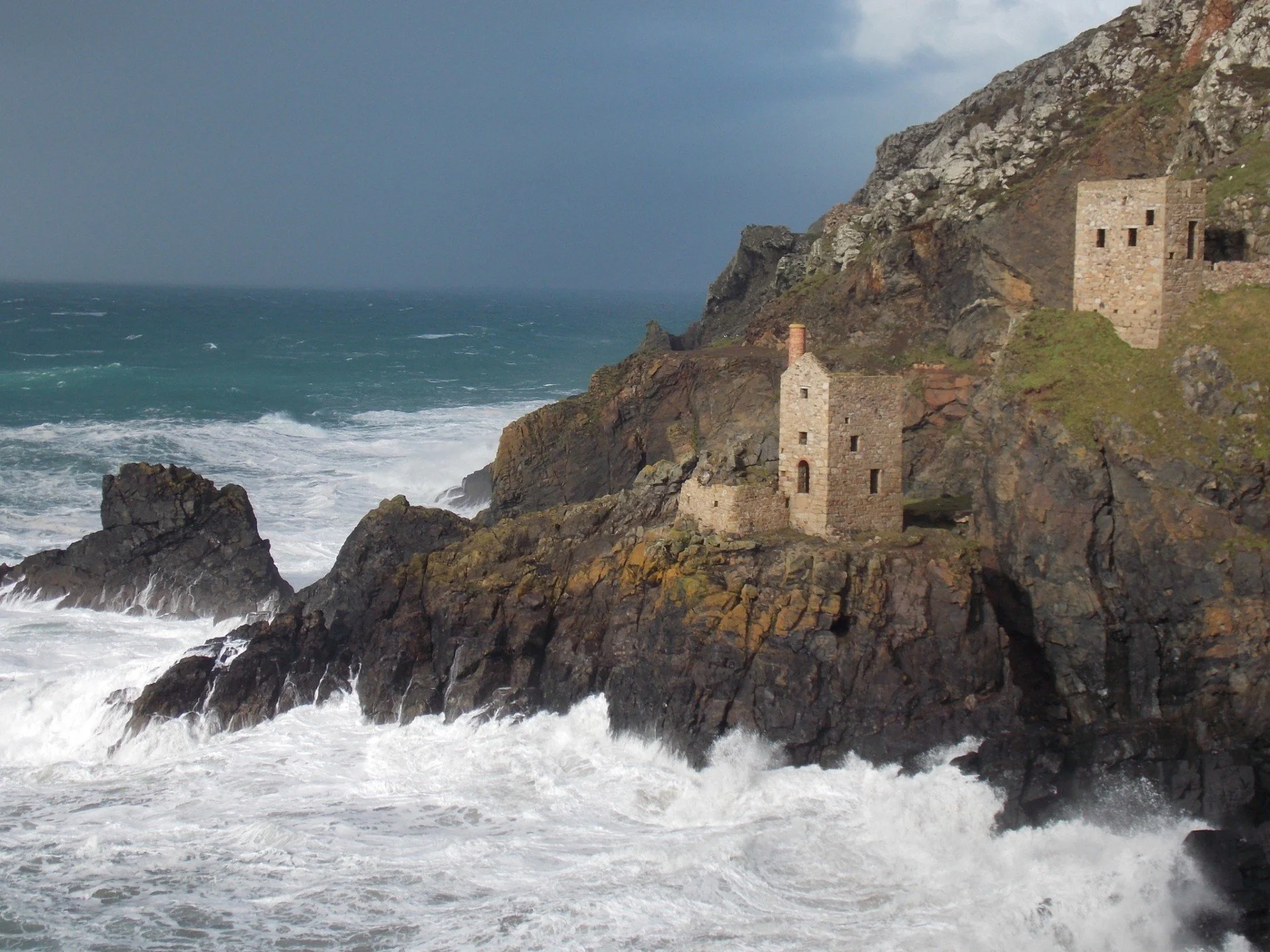 Cliffs along the coastline at Botallack with ruined engine houses and turbulent ocean waves crashing against rocks.