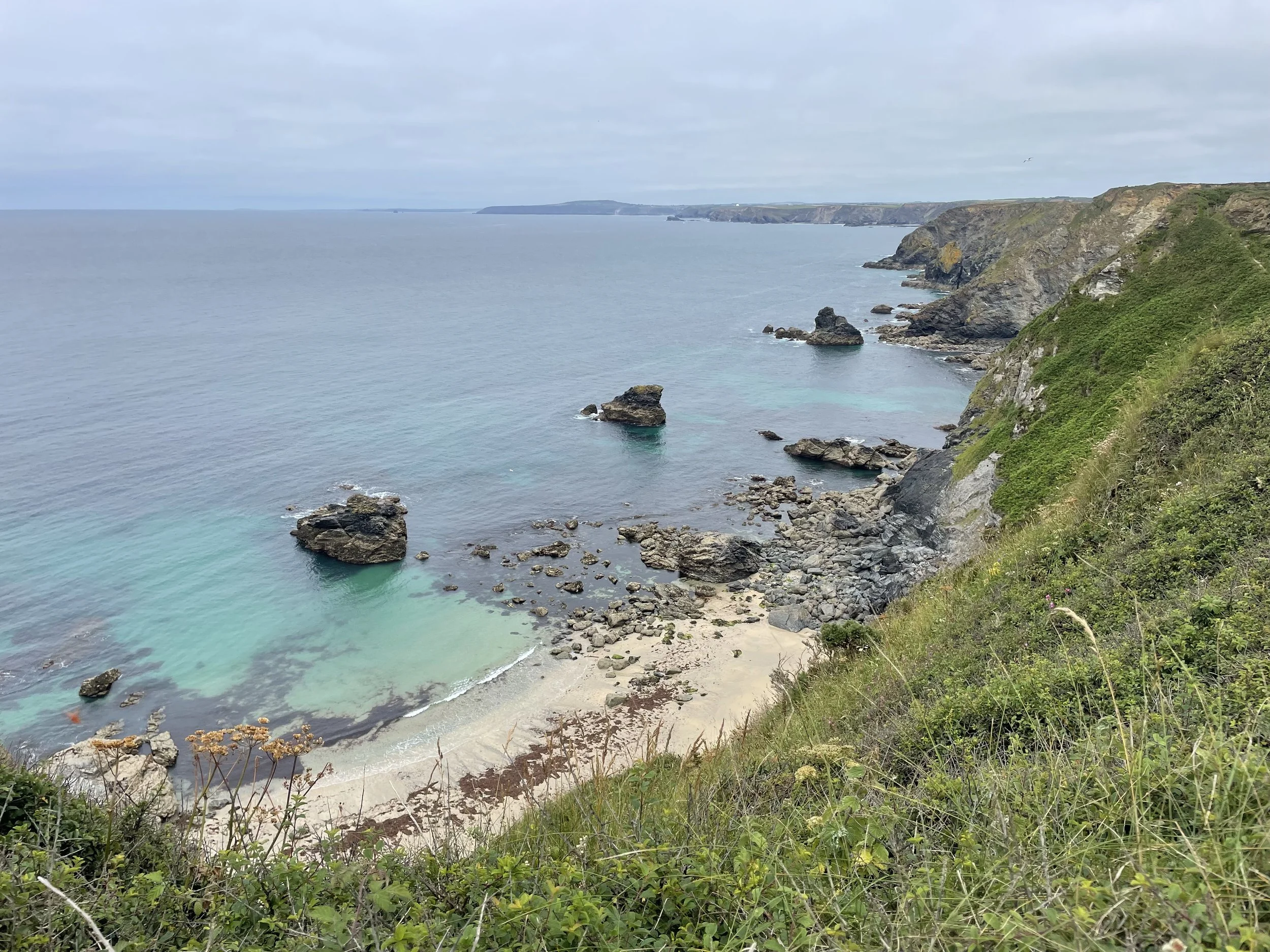 The North Cliffs coastal landscape with green vegetation, rocky shoreline, and calm ocean under cloudy sky.
