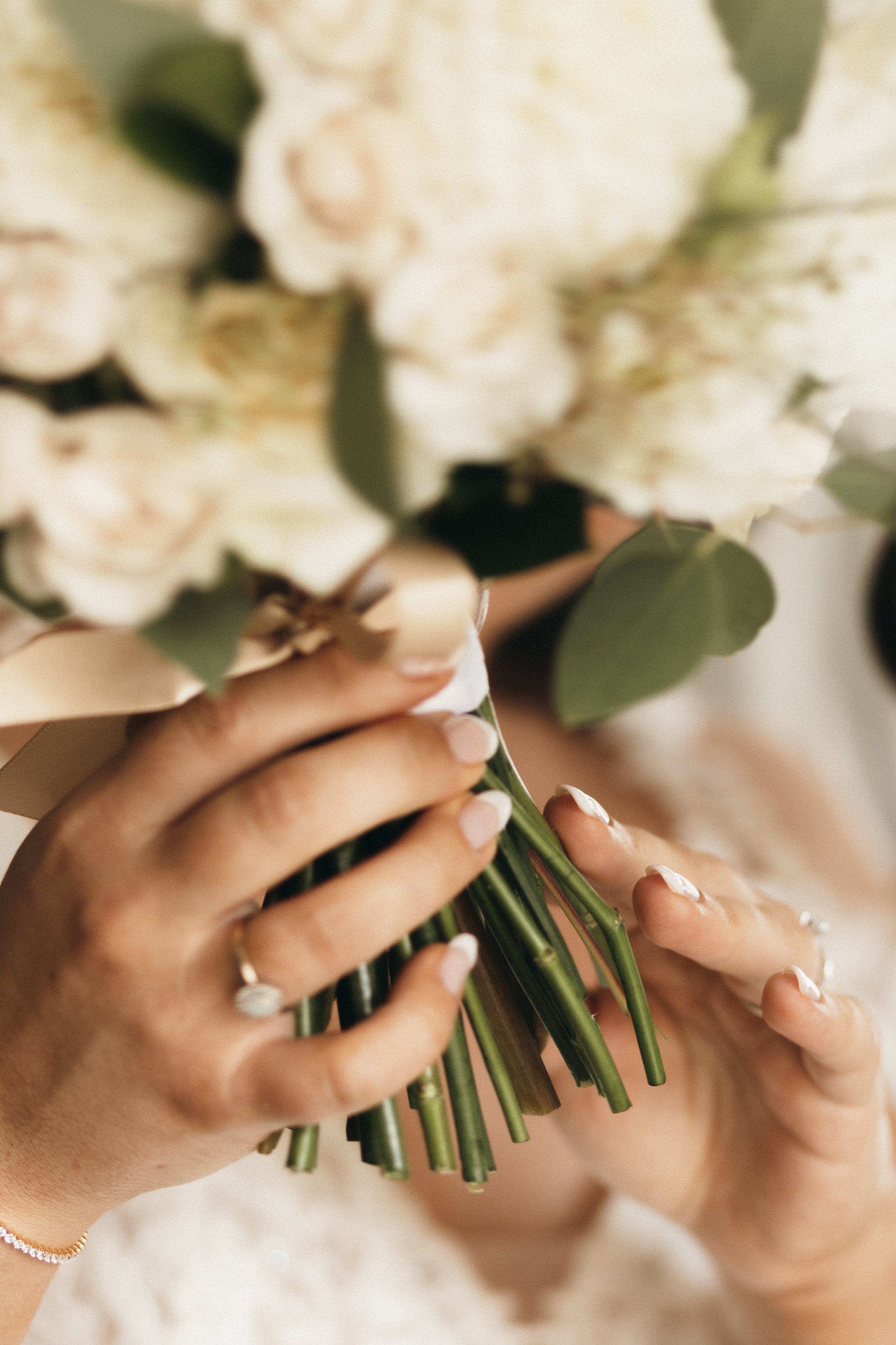 Close-up of hands holding a bouquet of white flowers with green leaves.