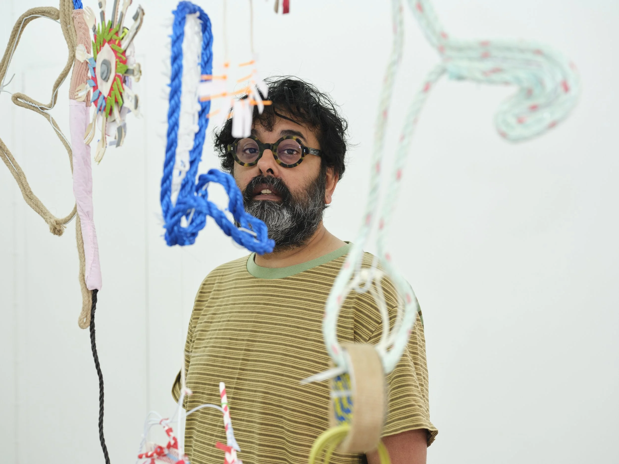 A man with glasses and a beard looking at colorful ropes hanging on a white wall.