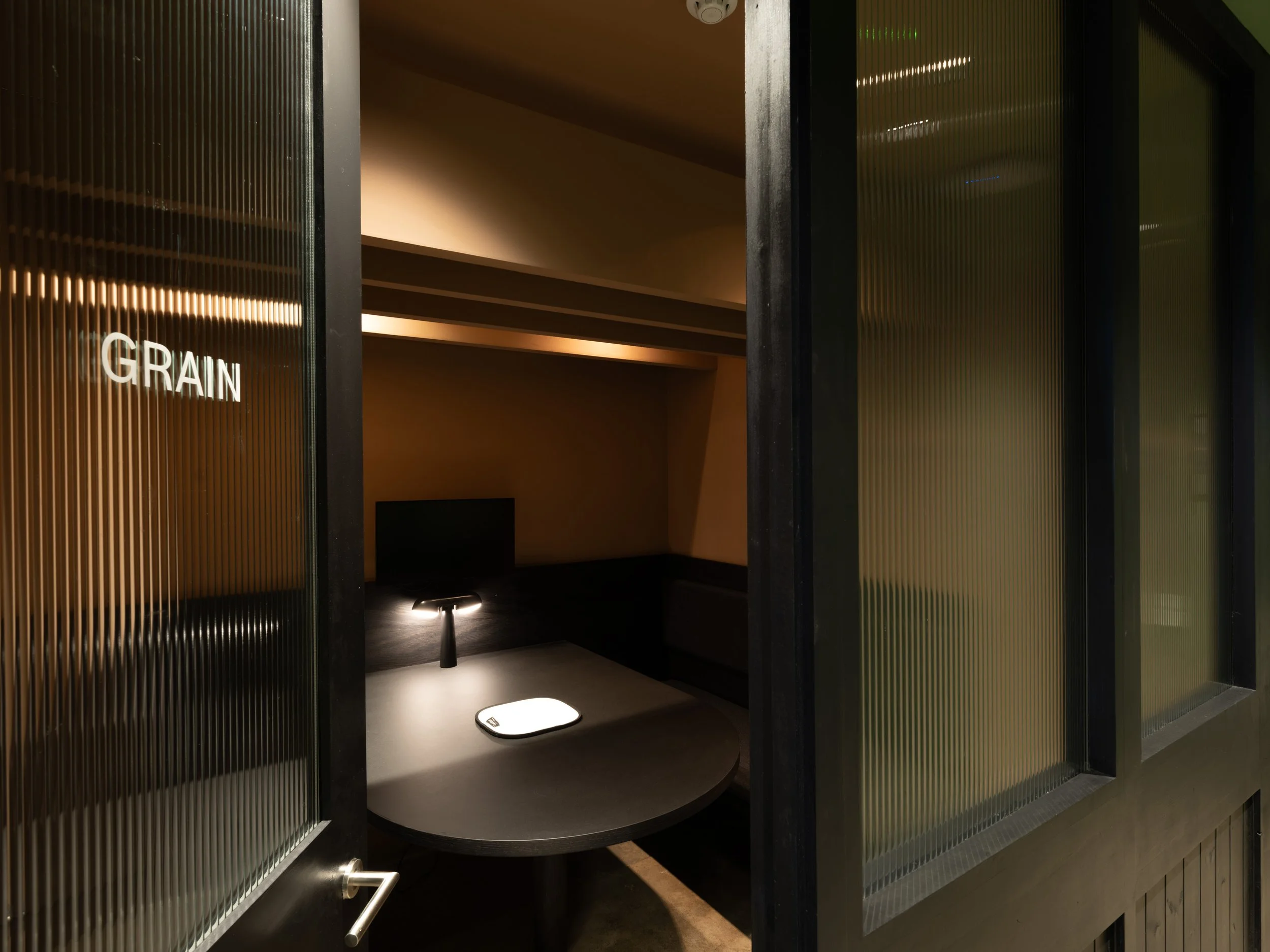 Interior of a modern, stylish grain storage or retail display area with black vertical framing, sliding glass doors, and warm lighting illuminating the space labeled 'GRAIN' with a digital scale in front.