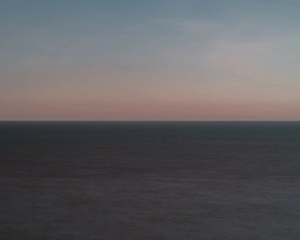A calm ocean under a pastel-colored sky at sunset or sunrise.