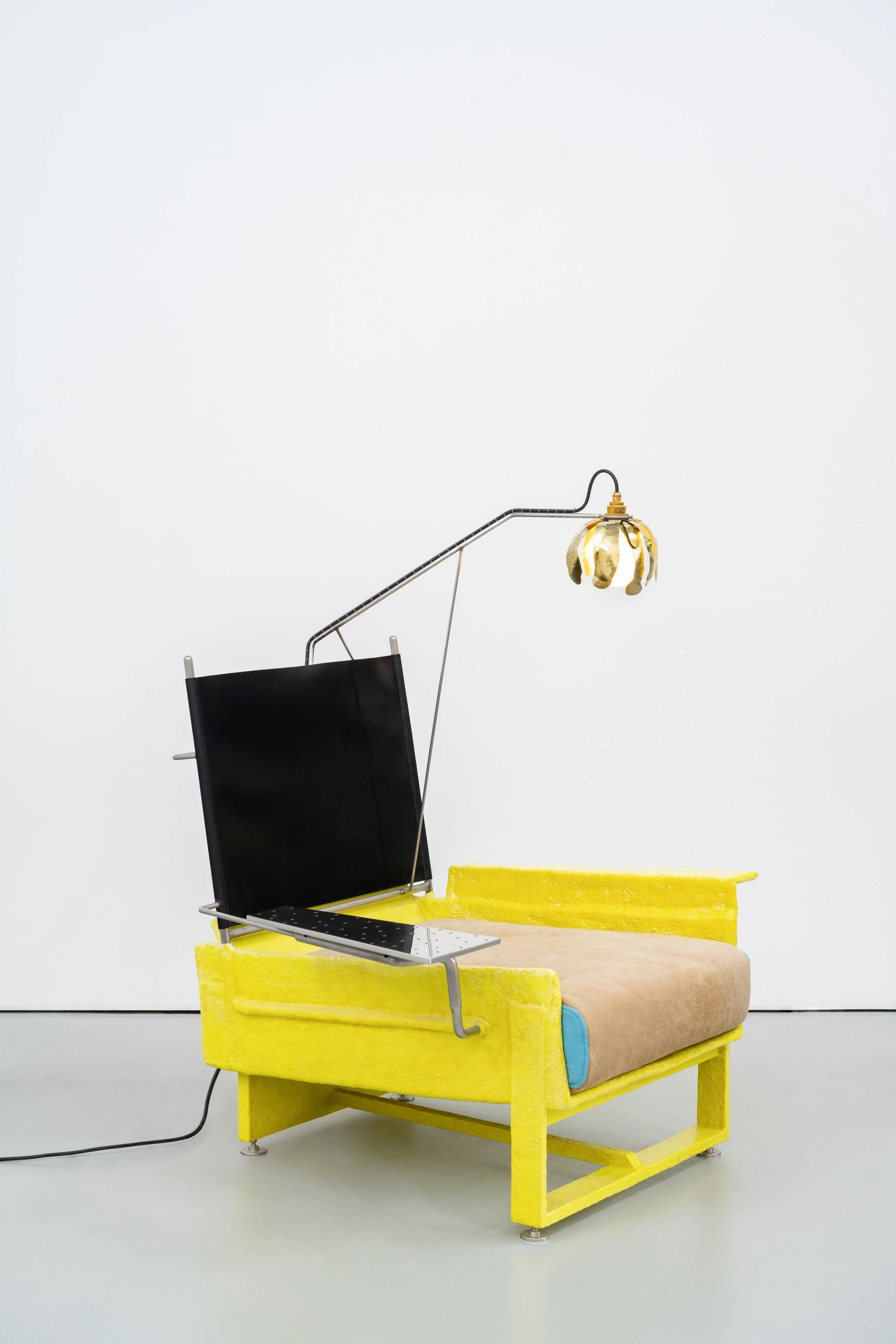 A yellow platform with a beige cushion holds a black office chair, a yellow box, and a small table, with a floor lamp featuring a gold floral lampshade.