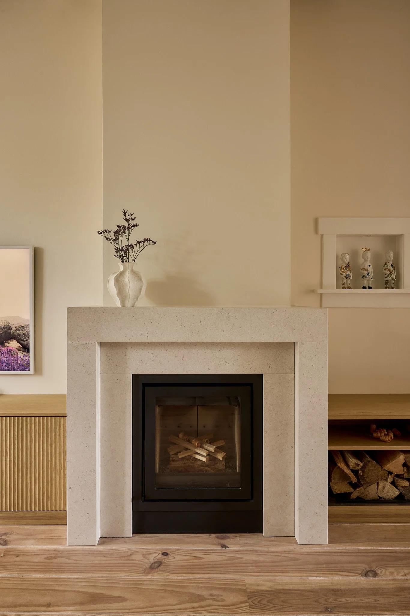 A cozy living room with a modern fireplace, decorative items on the mantel, and firewood stored on the right side.