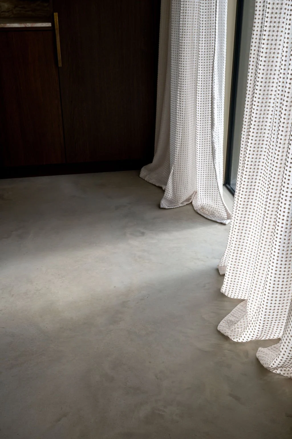 Empty room with beige carpet, dark wooden cabinet, and white polka dot curtains by a sliding glass door.