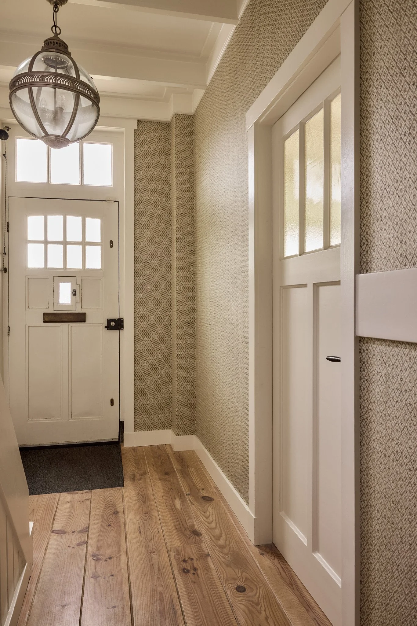 Entryway with a front door, patterned wallpaper, and wooden flooring.