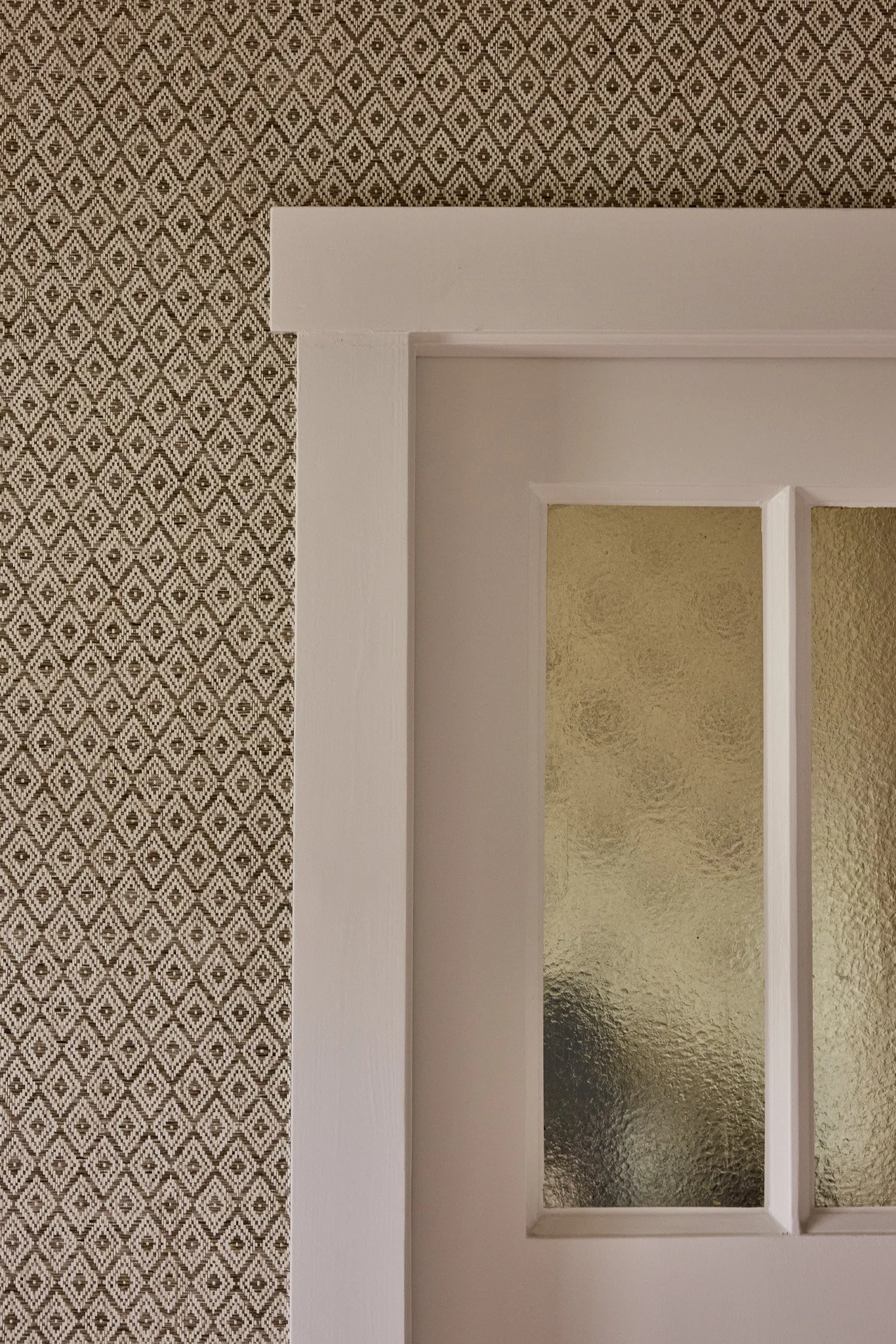Part of a door with white framing and textured glass panels, beside a wall with geometric patterned wallpaper in shades of brown and beige.