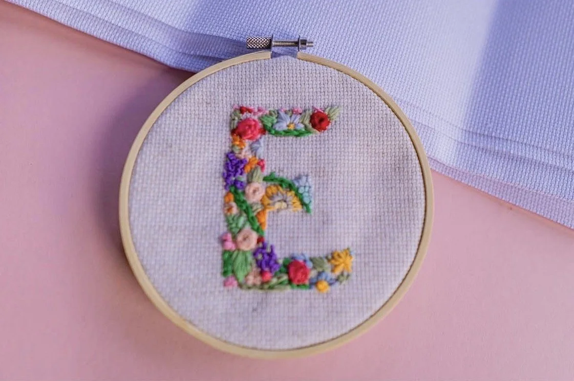 Embroidery hoop with a stitched letter 'E' decorated with colorful floral patterns.