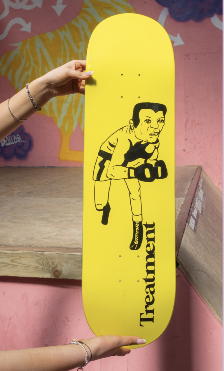 Yellow skateboard with a black line drawing of a man with short hair, sweating, wearing gloves and striped sportswear, and holding boxing gloves. The skateboard has the word "Treatment" written vertically in black letters.