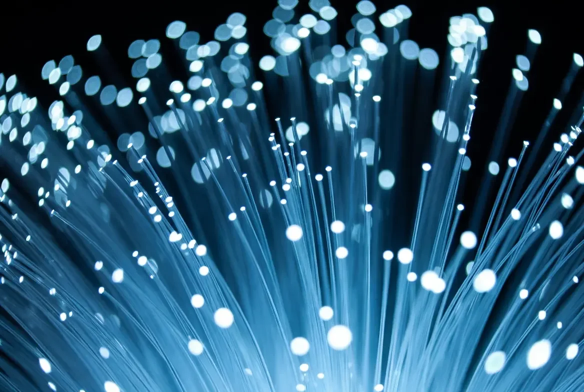 Close-up of fiber optic strands glowing blue with white dots of light.