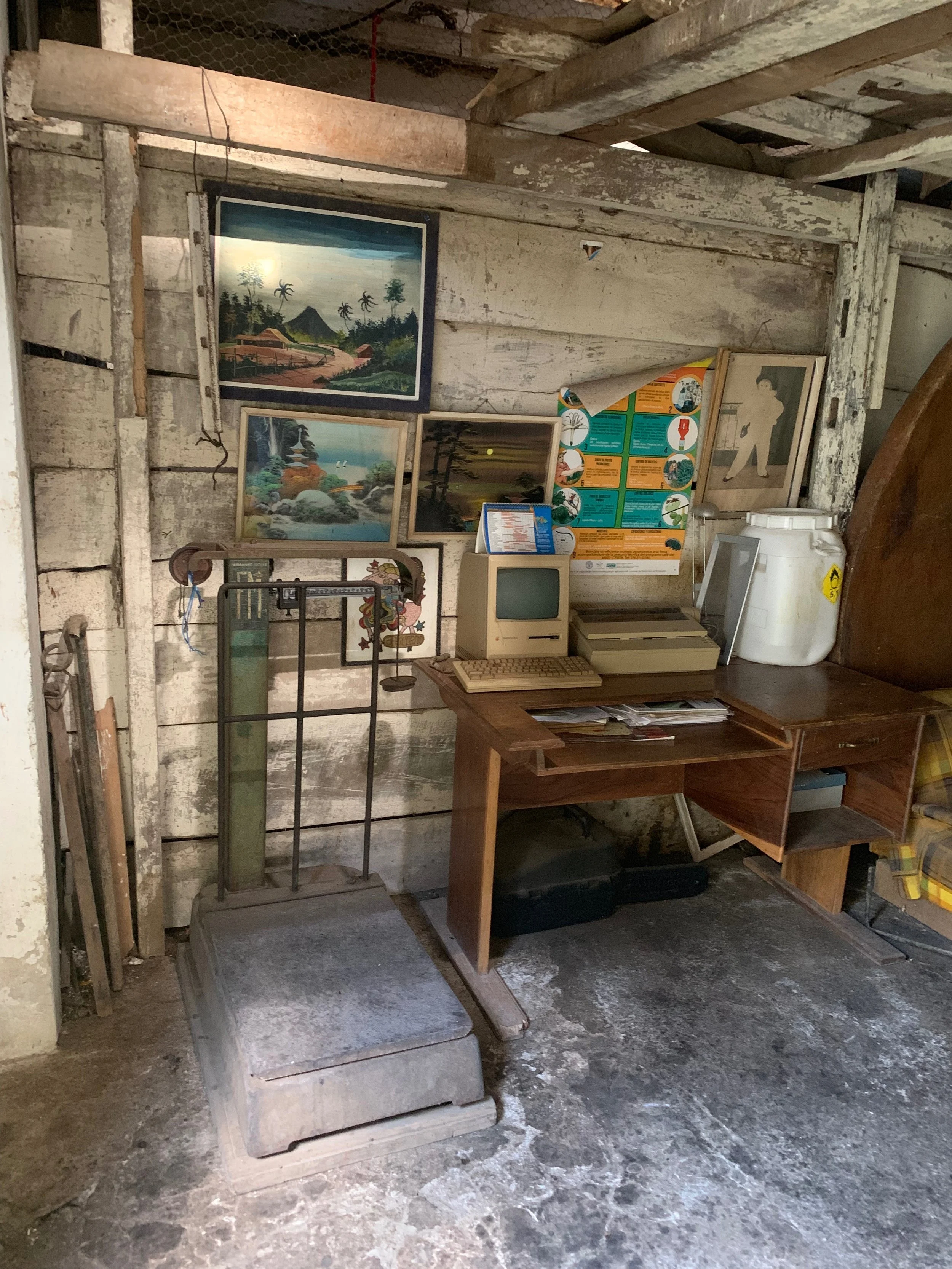 Alte, verlassene Werkstatt mit verschiedenen Bildern an der Wand, einem alten Computer, einem Waschbehälter und einem Holzschreibtisch.