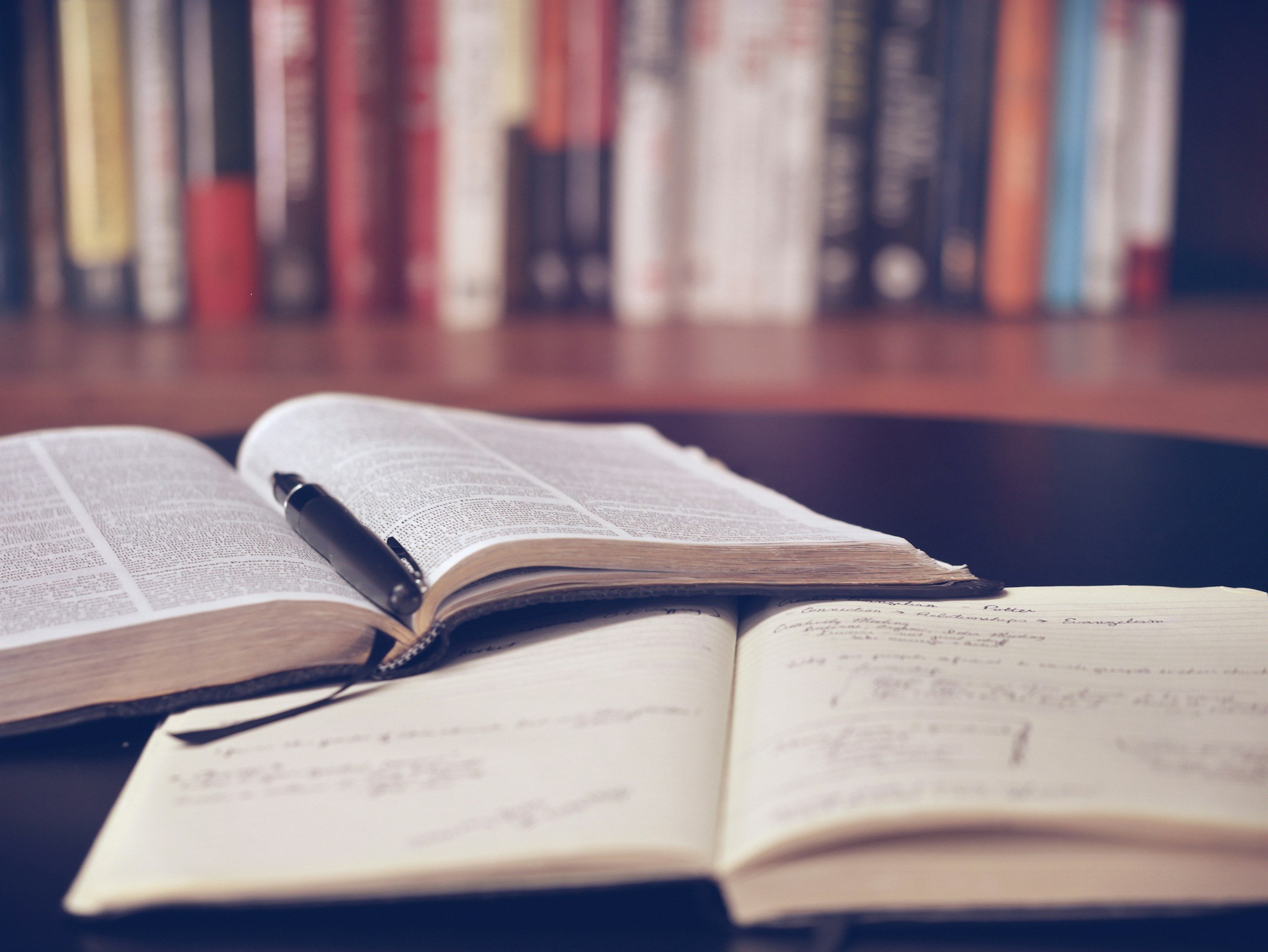 open book and a pen and an open notebook with books in the background