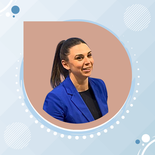 Portrait of a woman with a ponytail wearing a blue blazer against a neutral background.