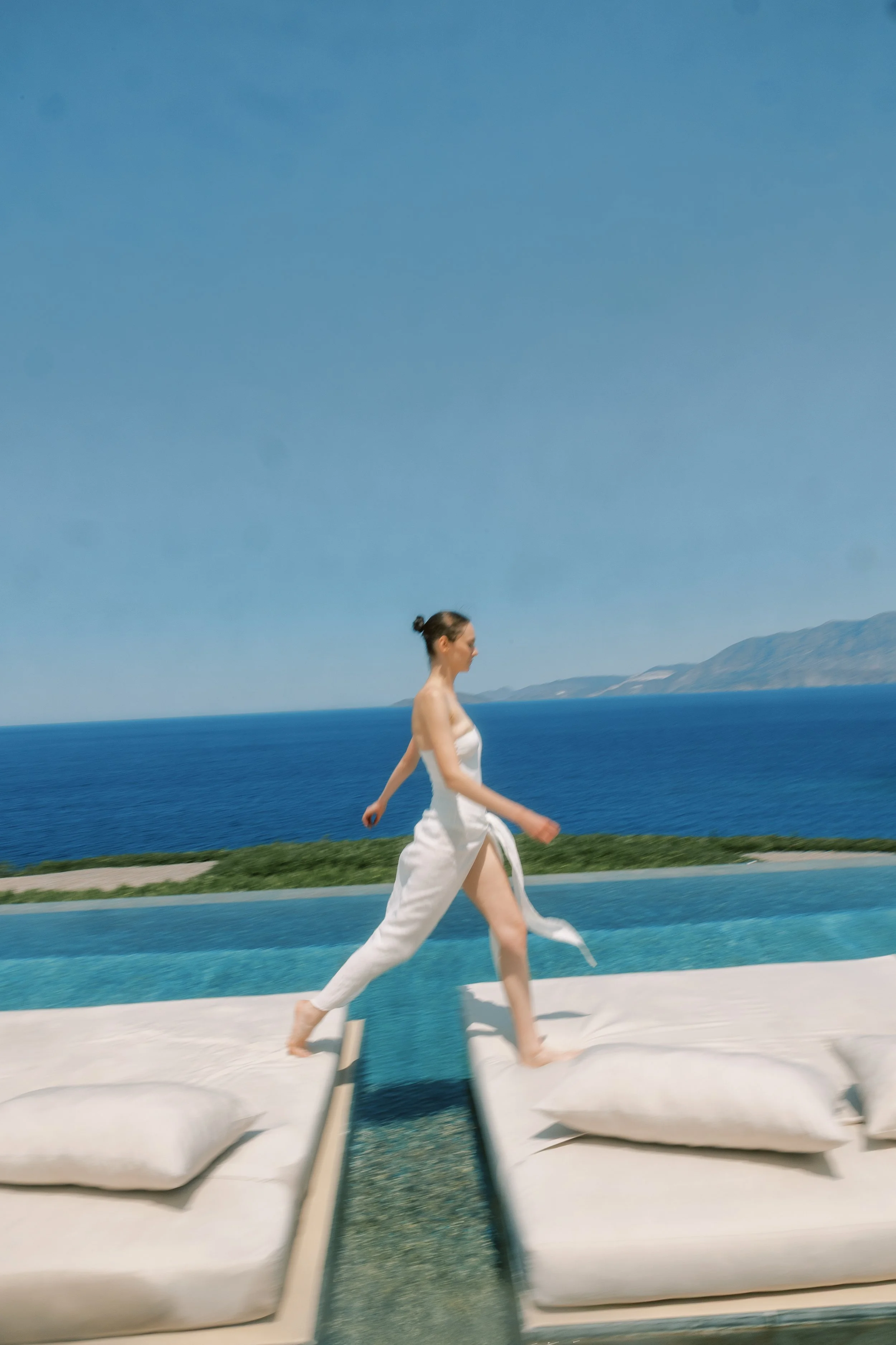 Bride in white walking across an infinity pool overlooking the Greek sea