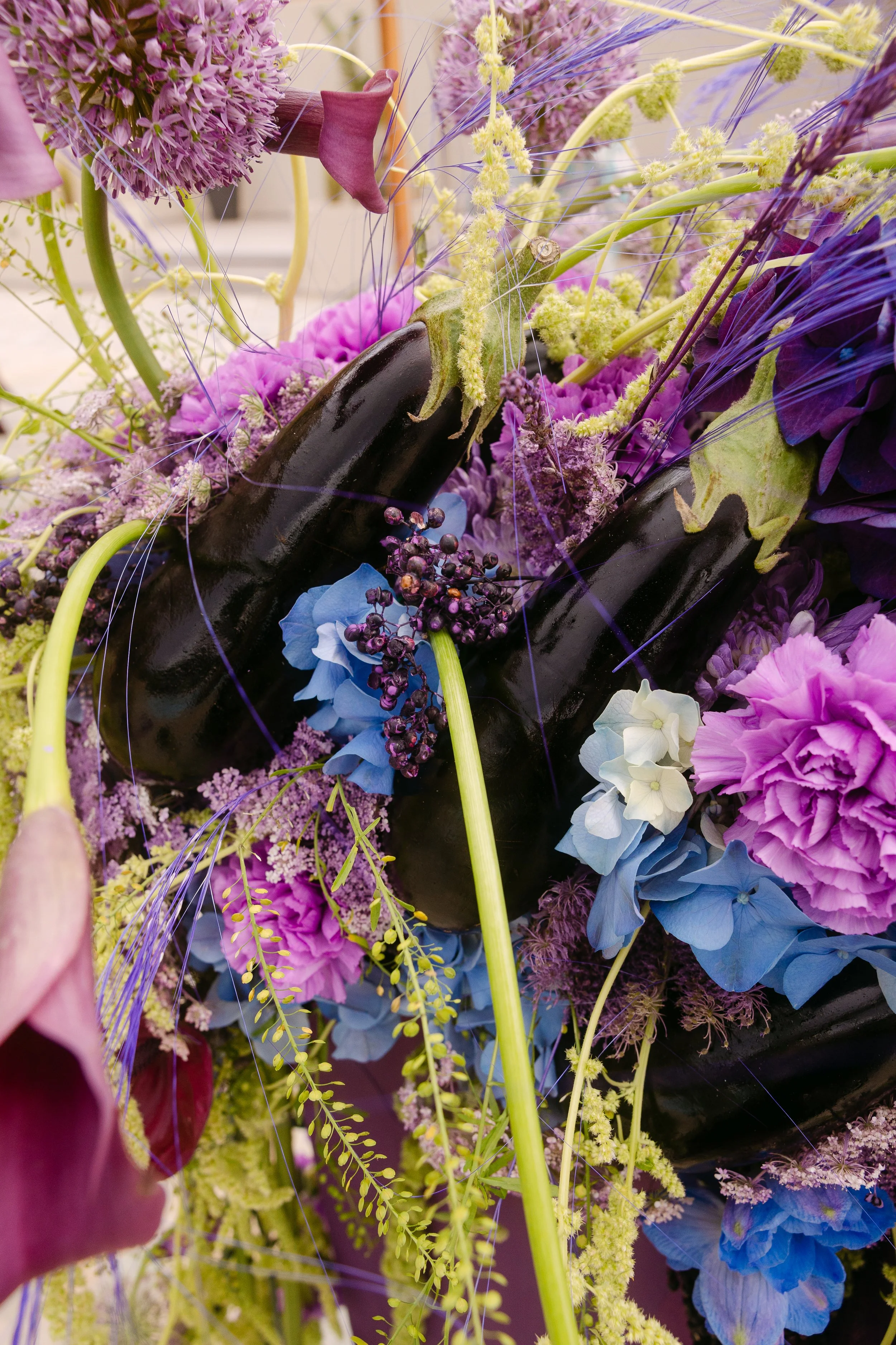 Abundant wedding table flowers in violet, magenta, blue and green with textural grasses.
