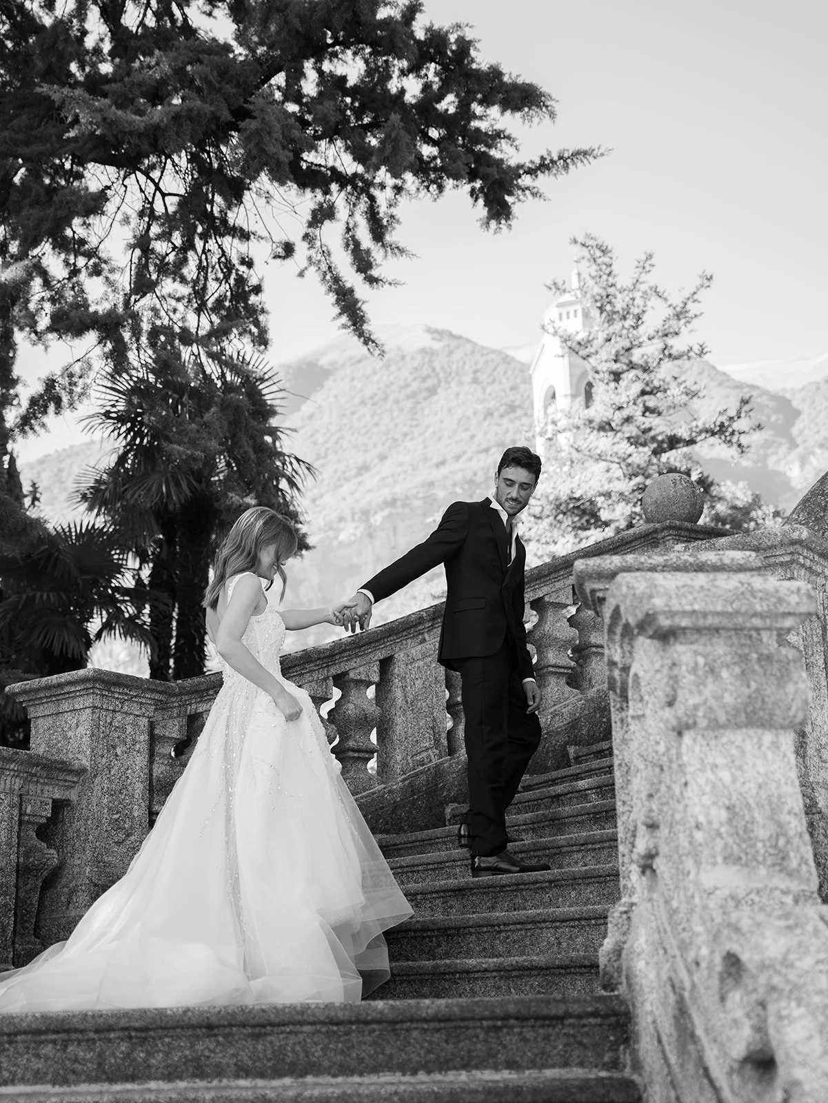 Black-and-white photograph of a couple walking down an ornate stone staircase during an intimate Lake Como elopement.