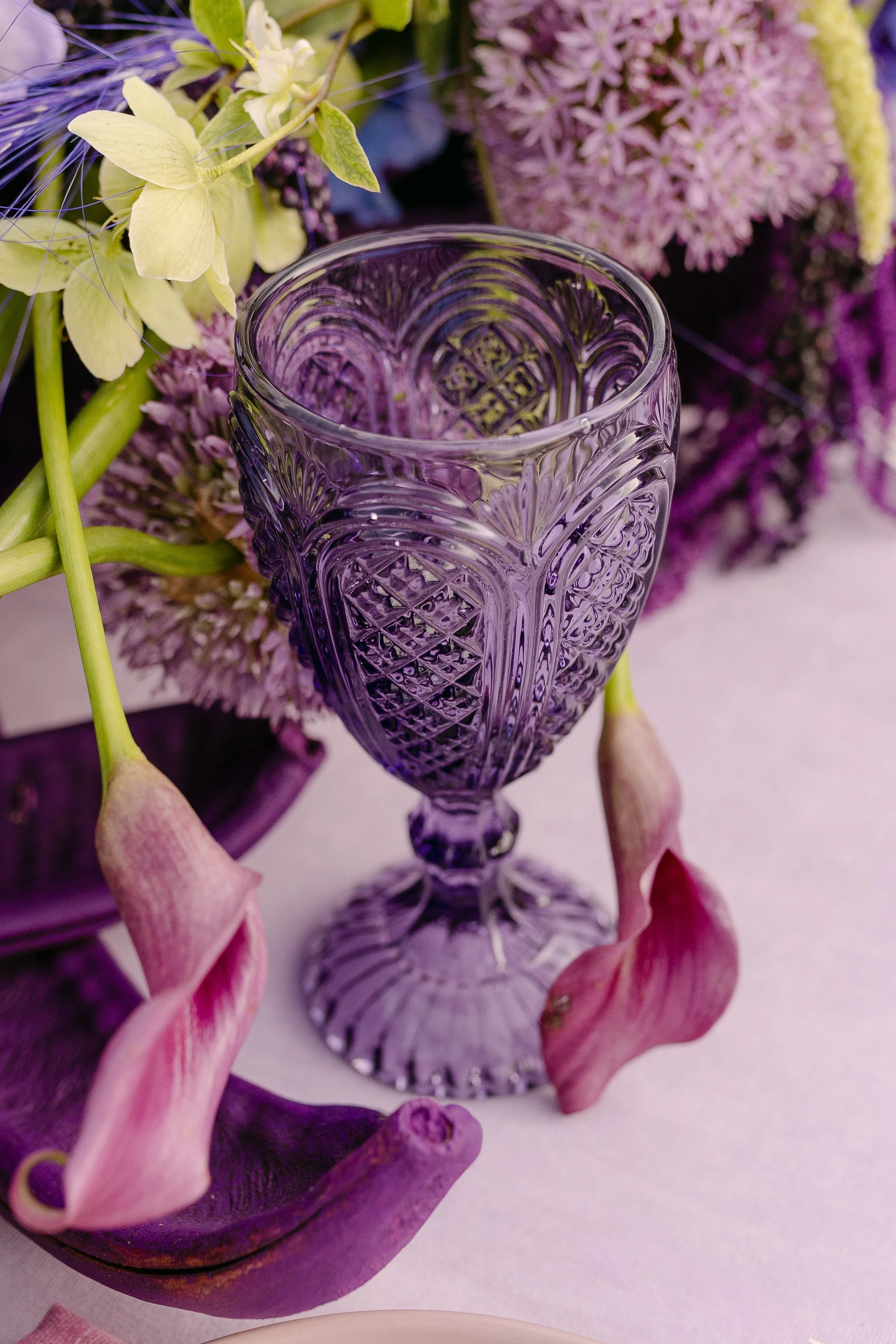 Ornate smoky purple wedding glassware surrounded by sculptural florals in violet and green.