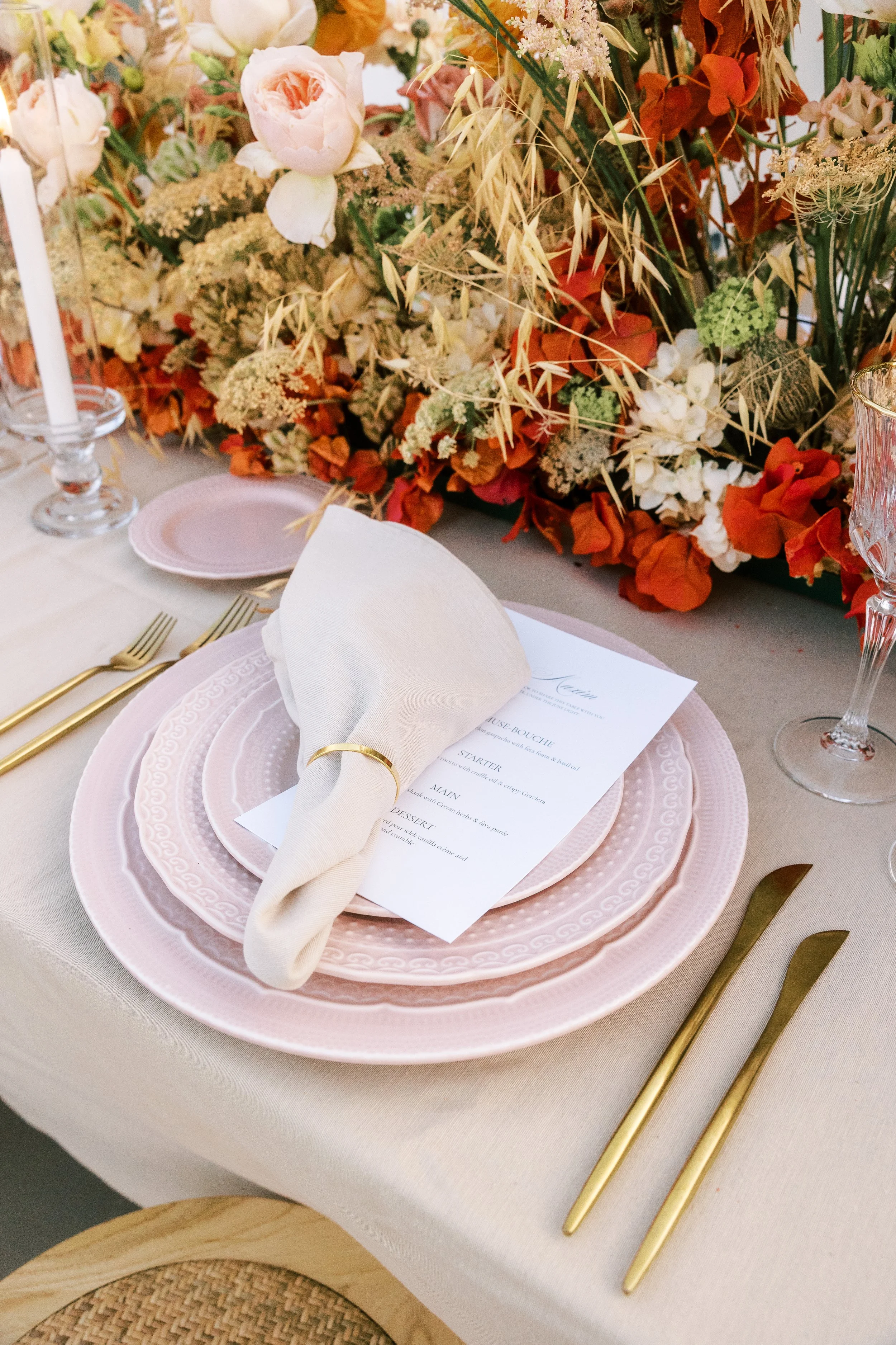 Refined wedding place setting with soft pink tableware, gold cutlery and floral details in Crete.