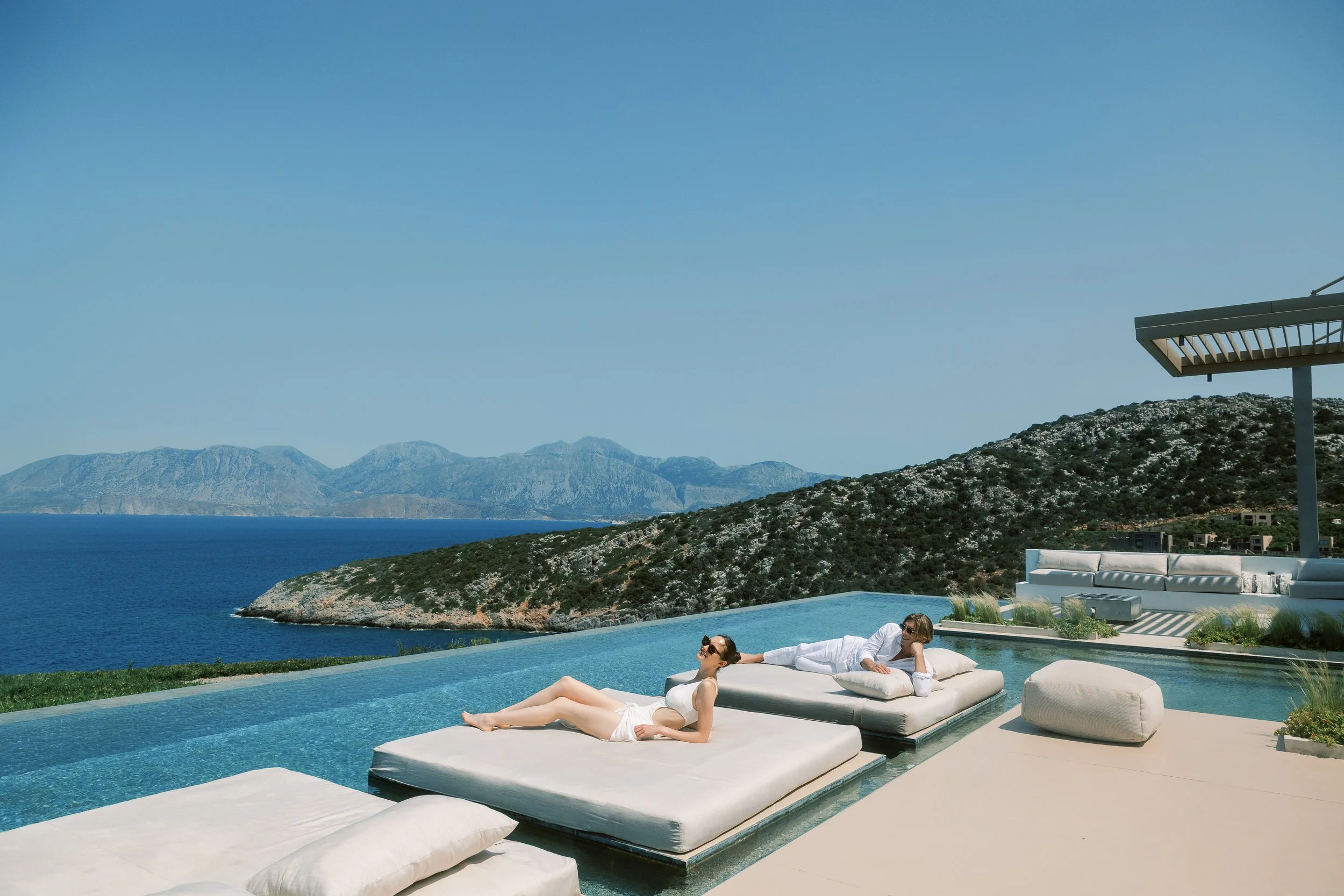 Couple relaxing beside an infinity pool during a multi-day wedding celebration in Crete.