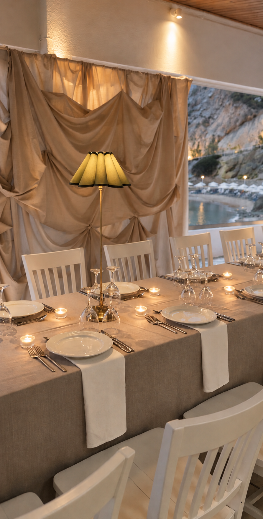Candlelit wedding dinner table with draped linen and lamplight above the sea at dusk