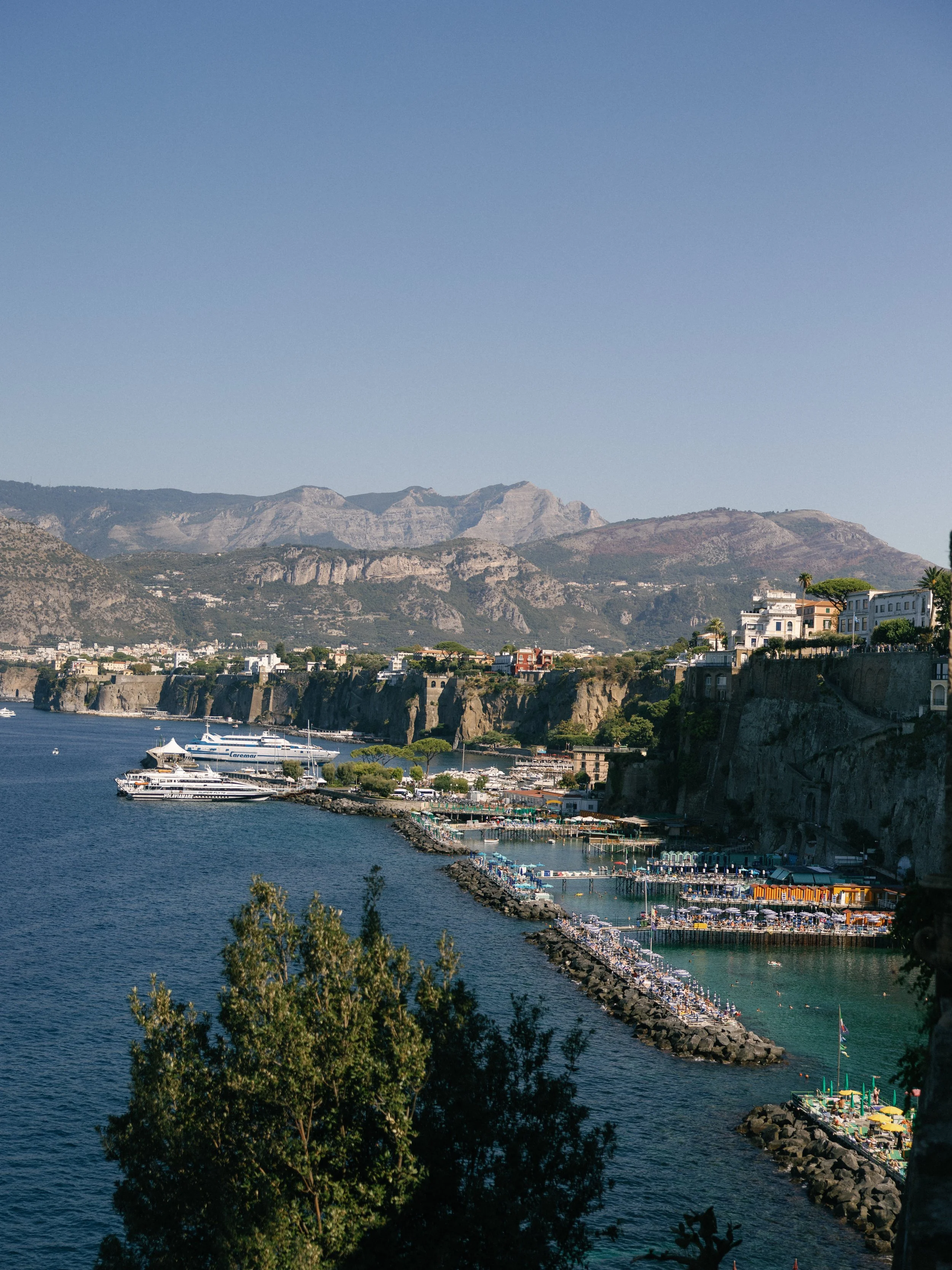 Sorrento waterfront with boats, beach platforms and buildings above the coastal cliffs in Italy.