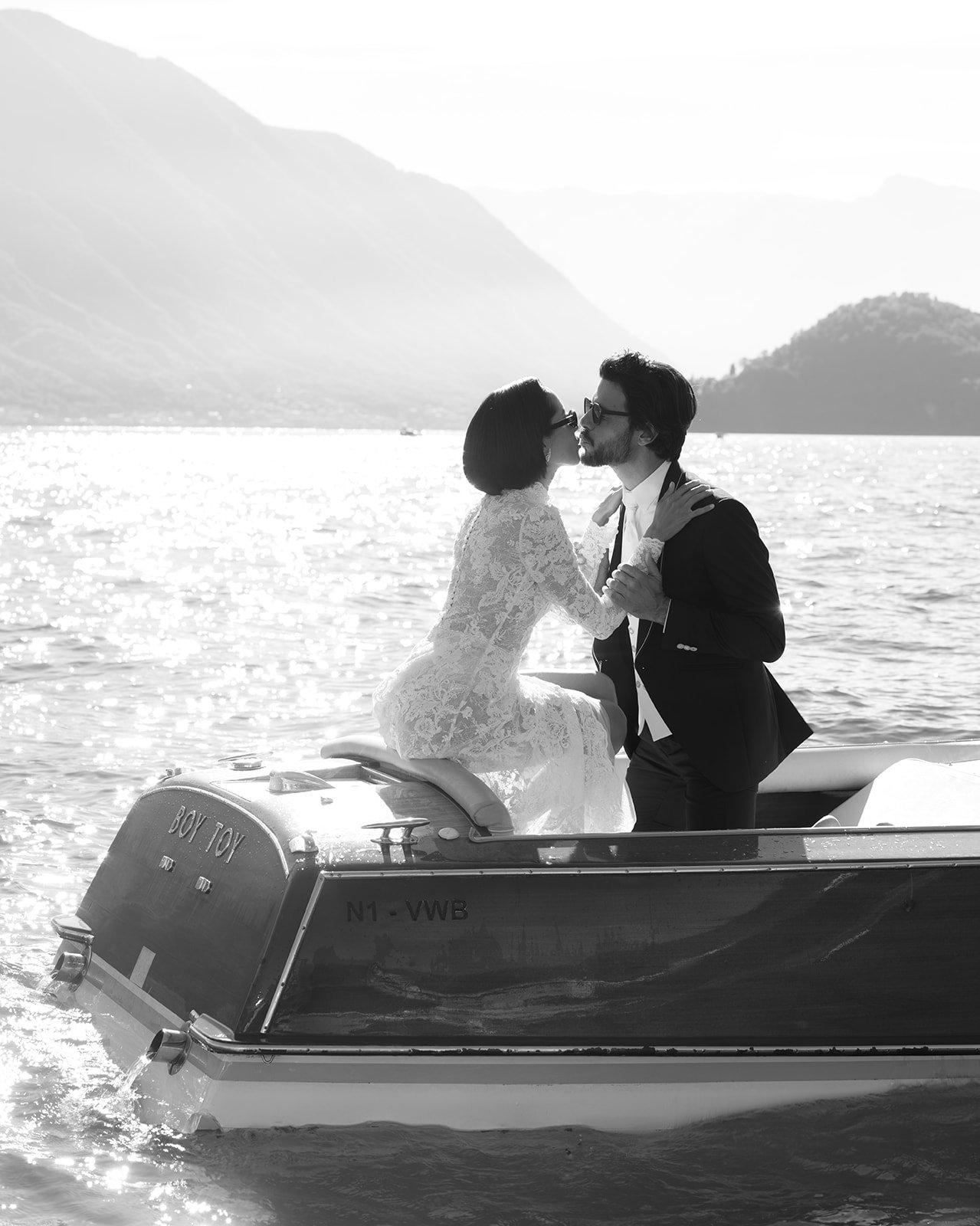 Black-and-white portrait of a bride and groom on a boat with the Lake Como mountains behind them.