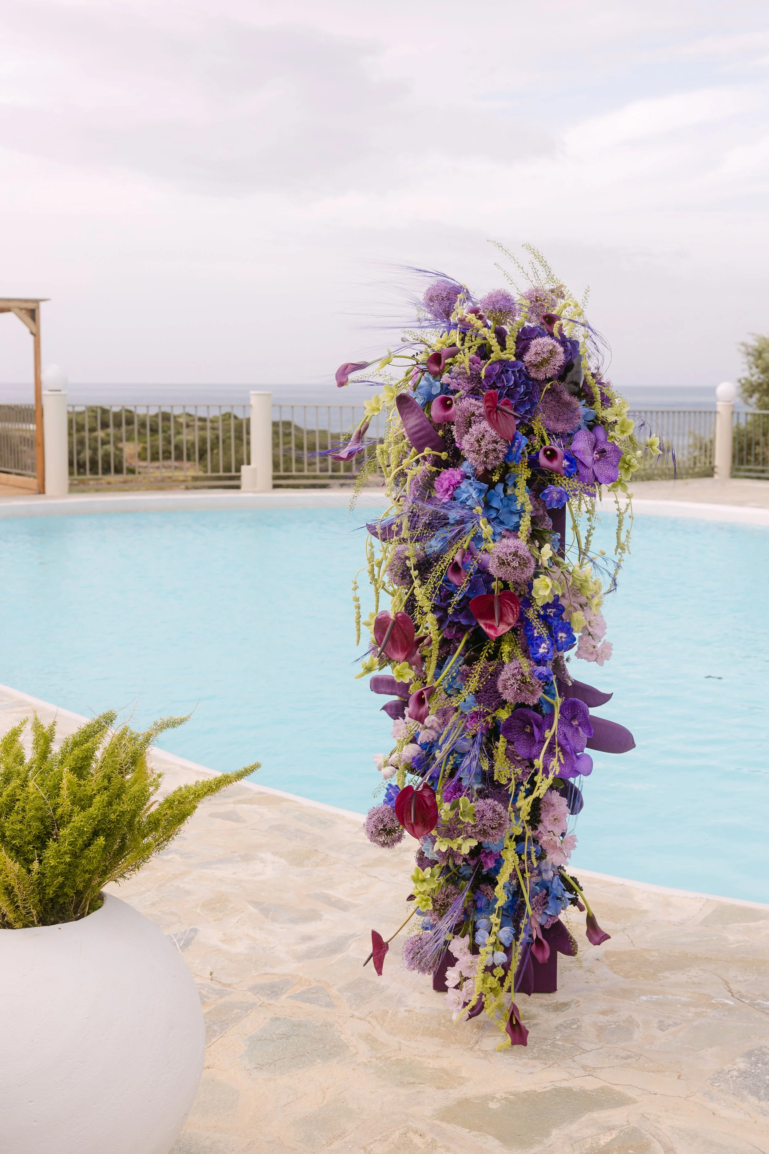 Sculptural floral column in violet, blue and pink beside the pool at a wedding in Crete.