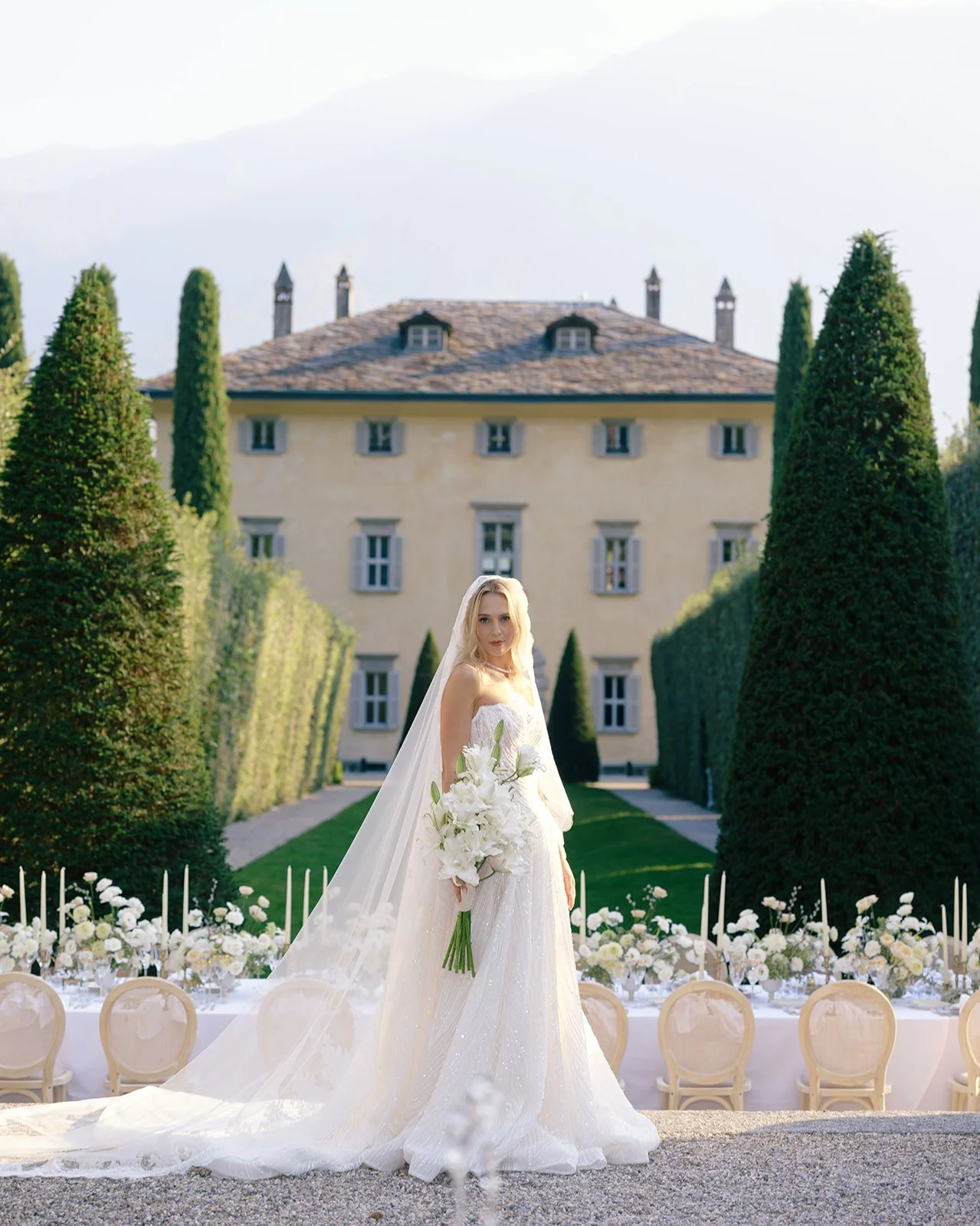 Bride standing before the historic villa balbiano surrounded by formal gardens and tall cypress trees.