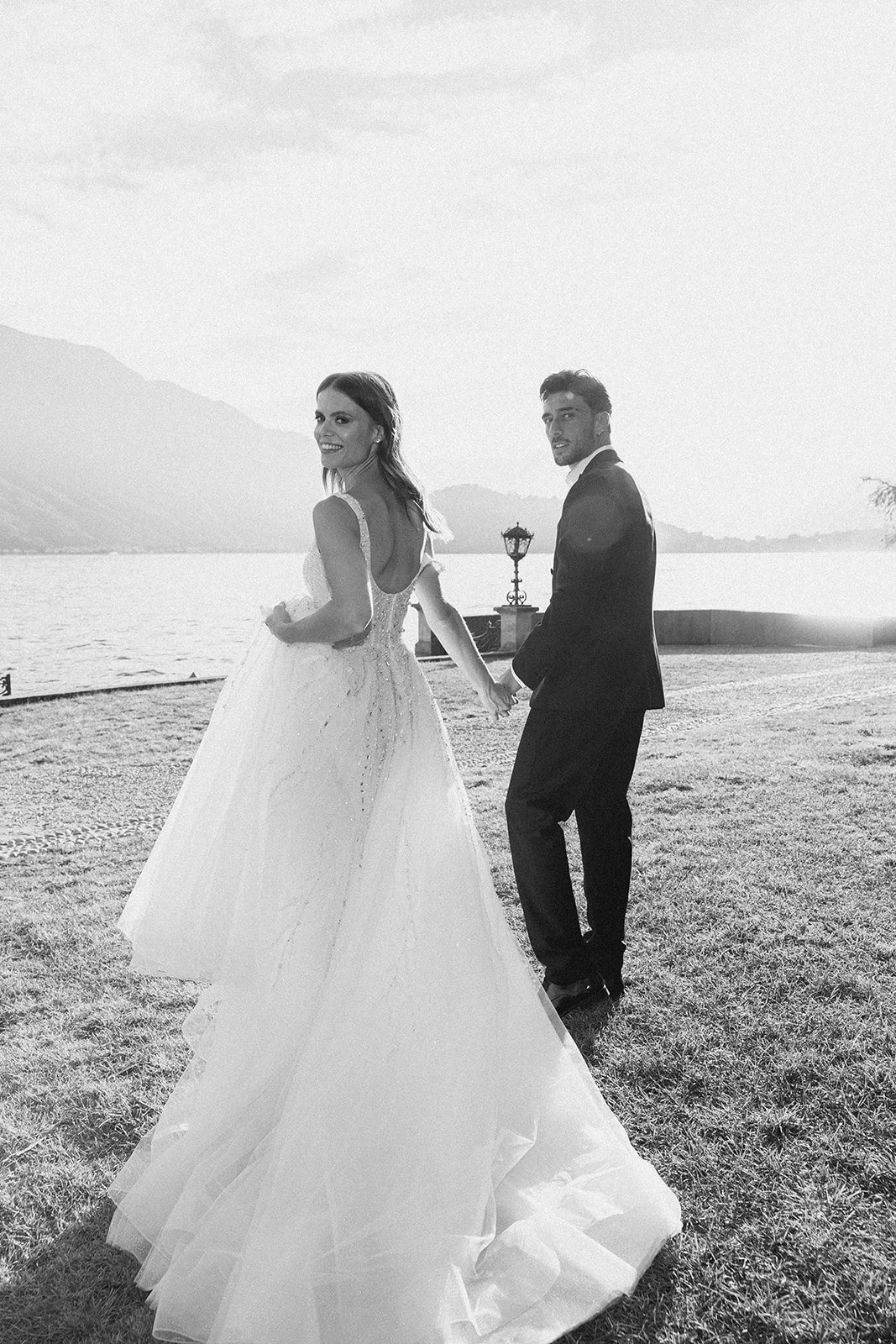 Black-and-white portrait of newlyweds walking beside Lake Como after their wedding ceremony.