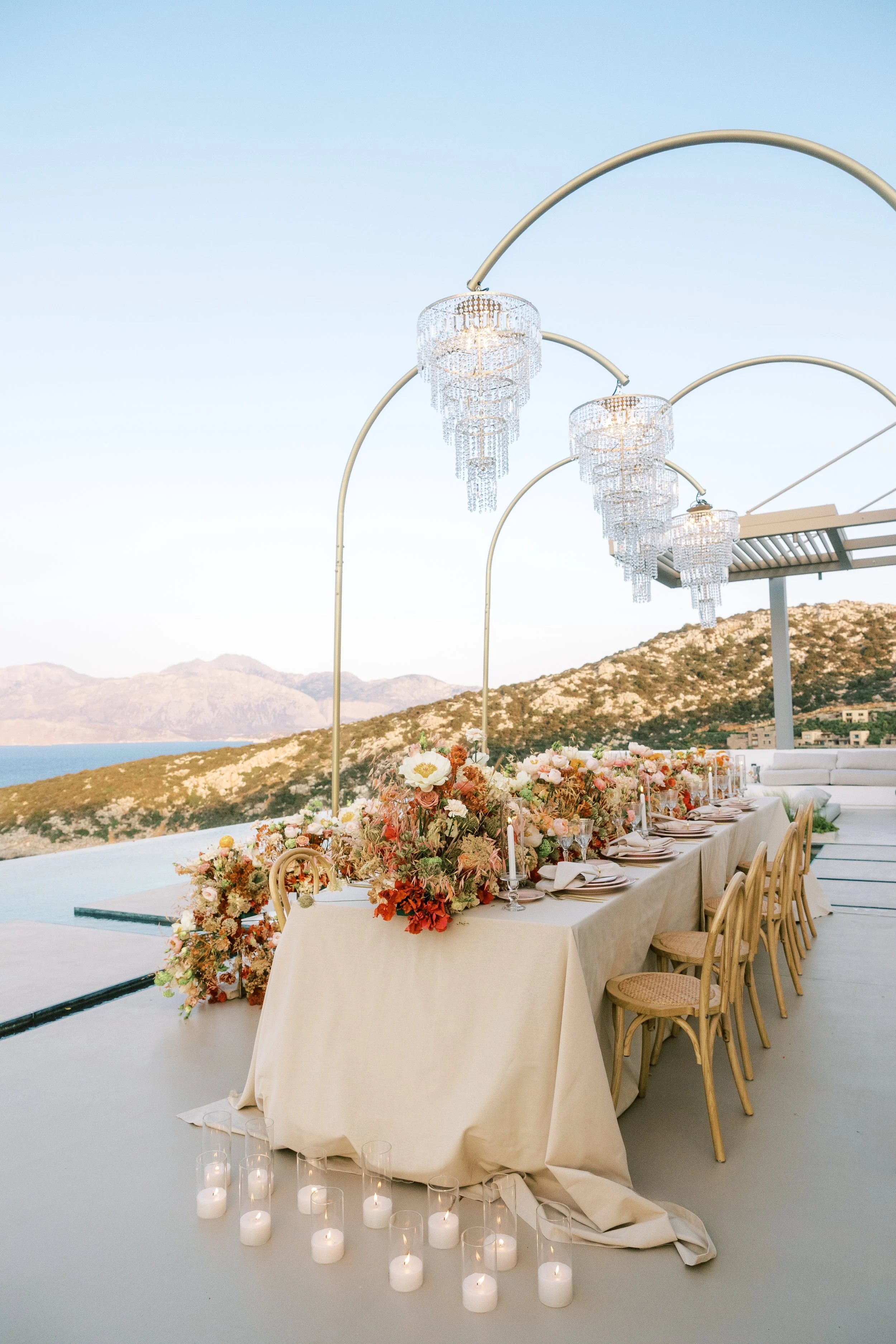 Outdoor wedding reception table with colourful flowers, candles and suspended crystal chandeliers in Crete.
