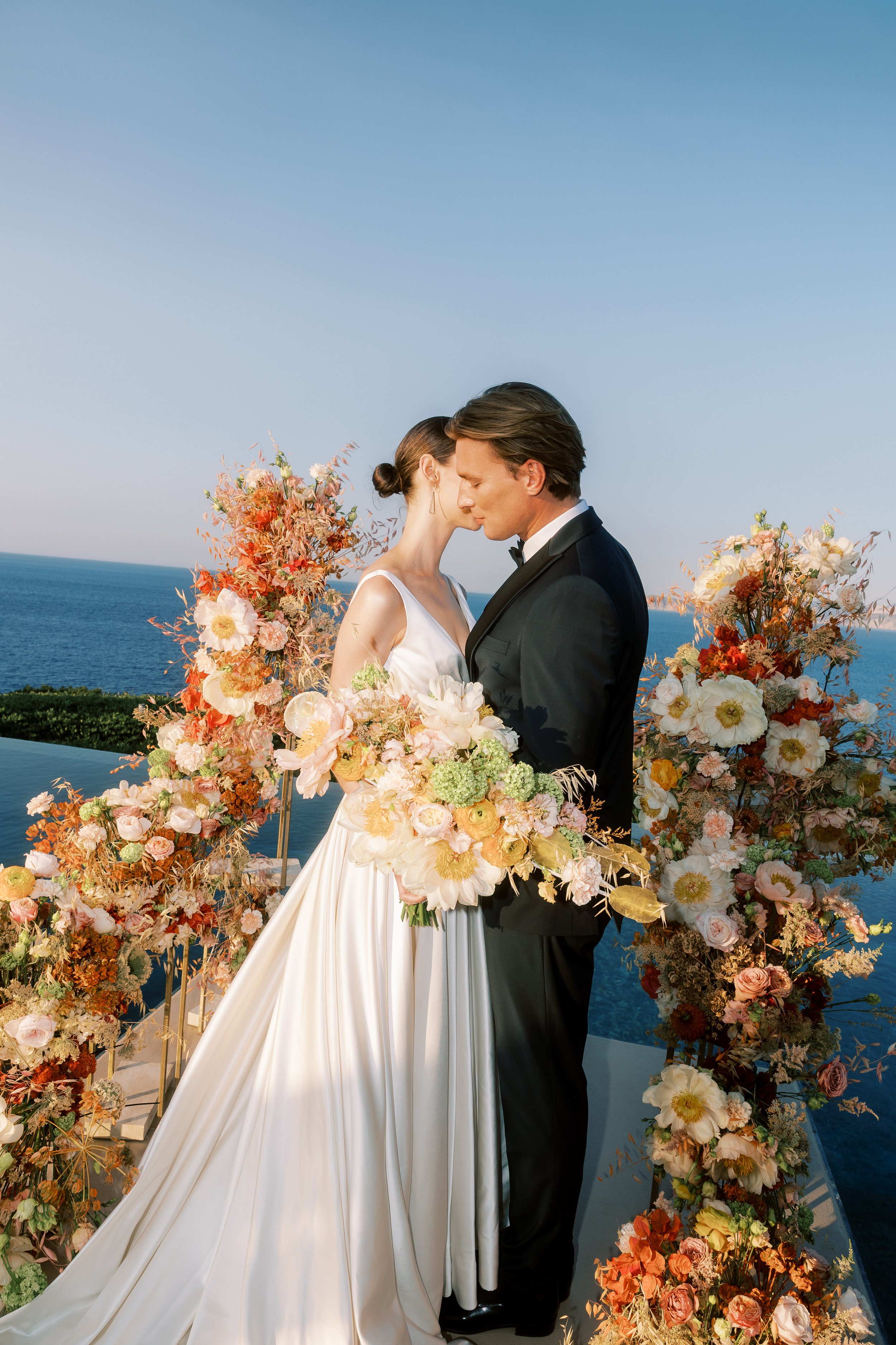Bride and groom surrounded by sculptural floral arrangements at a private estate wedding in Crete.