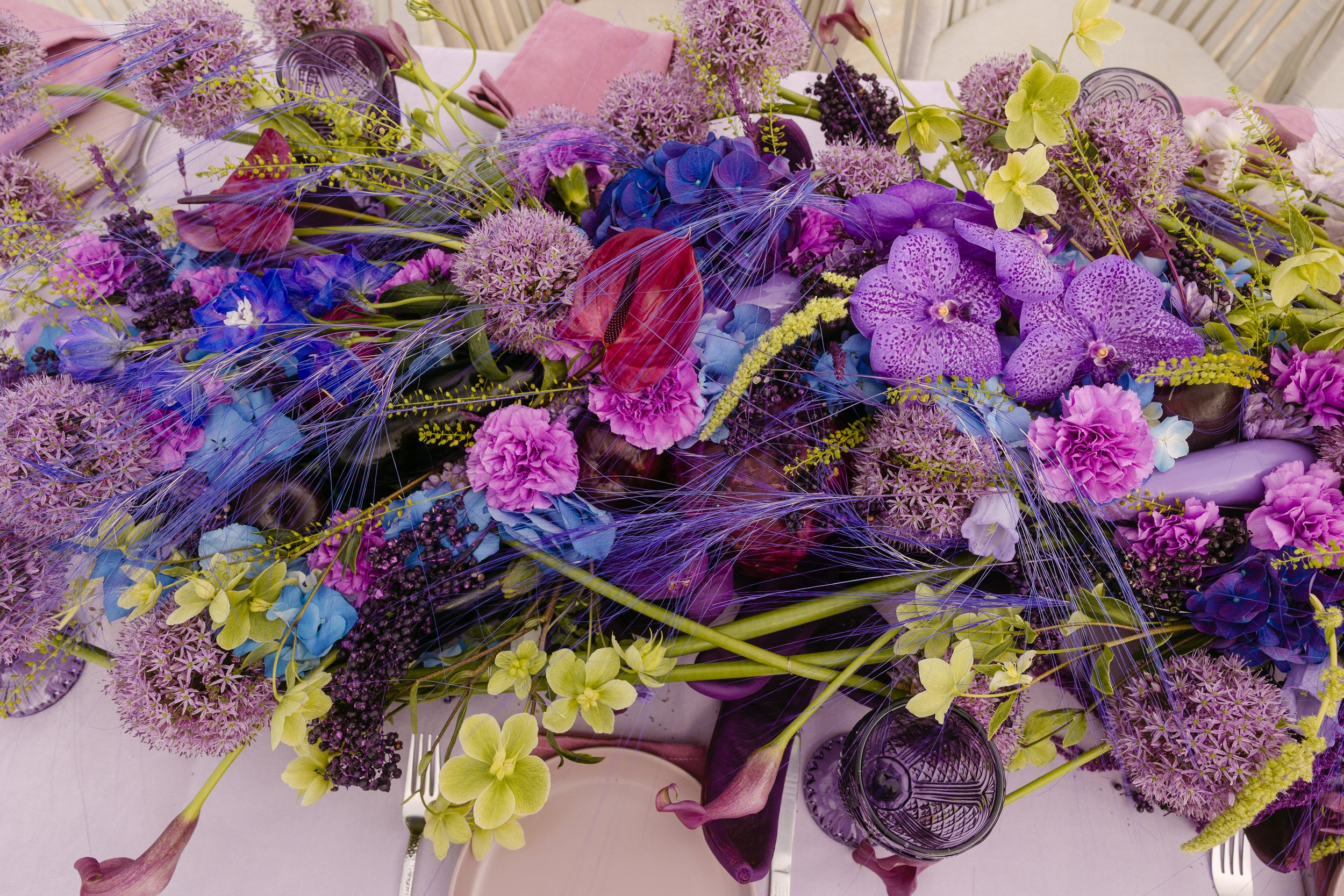 Colourful wedding floral arrangement with purple orchids, alliums, blue hydrangeas and trailing textures.