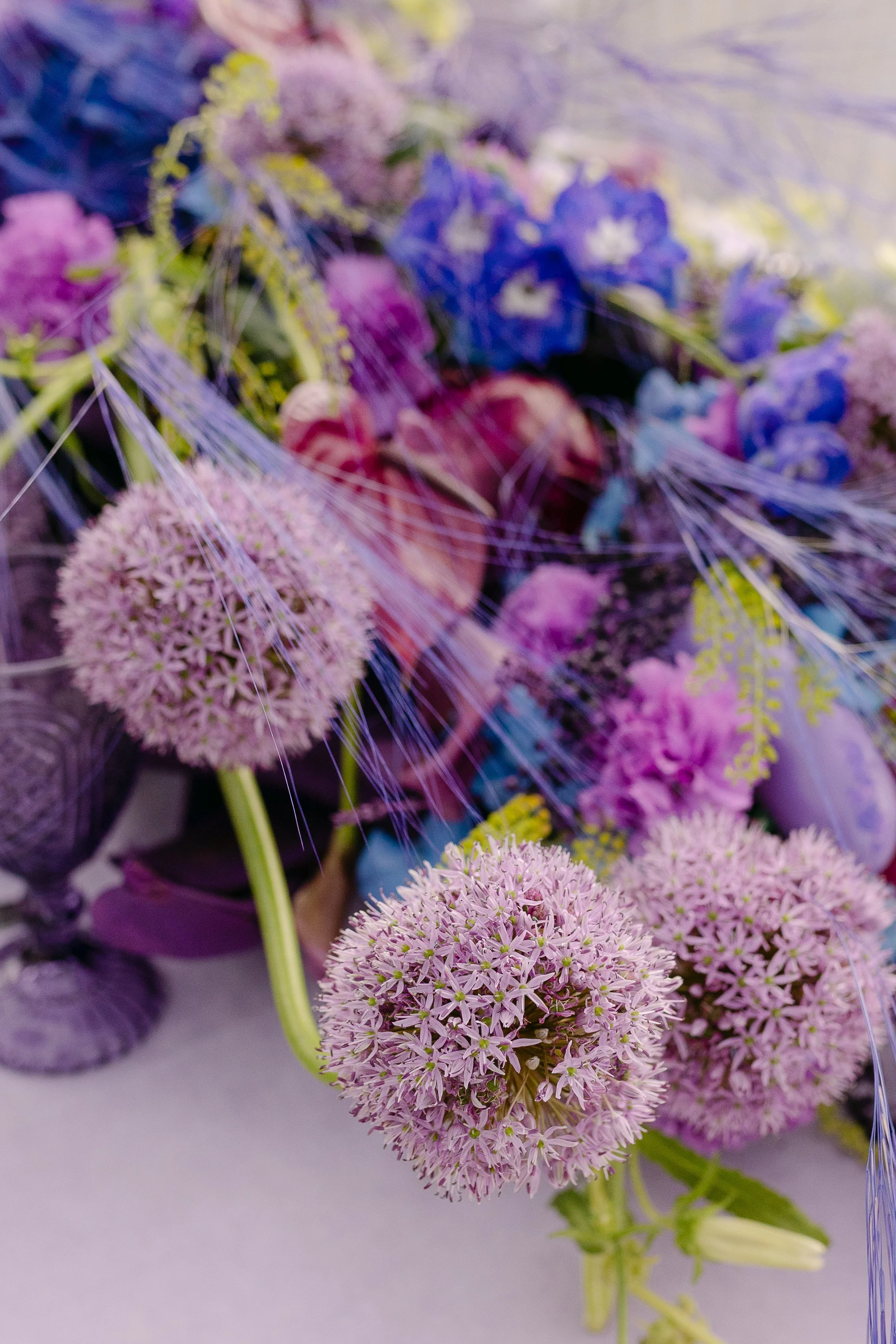 Close-up of purple alliums, blue flowers and textural grasses within a bold wedding floral arrangement.