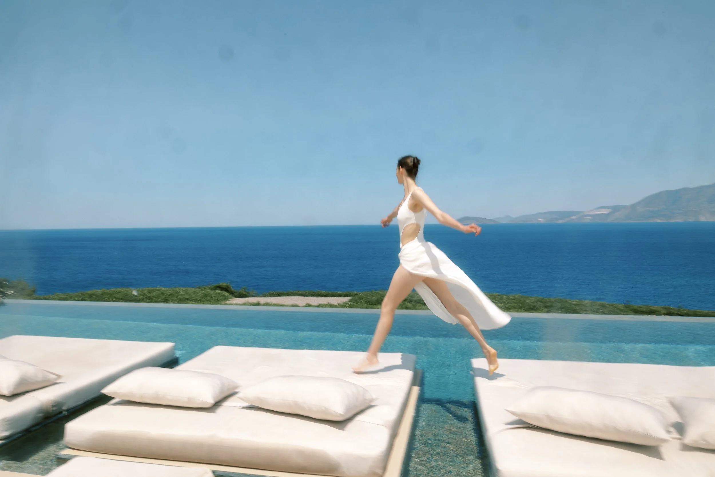 Bride walking beside an infinity pool at a contemporary private estate in Crete.