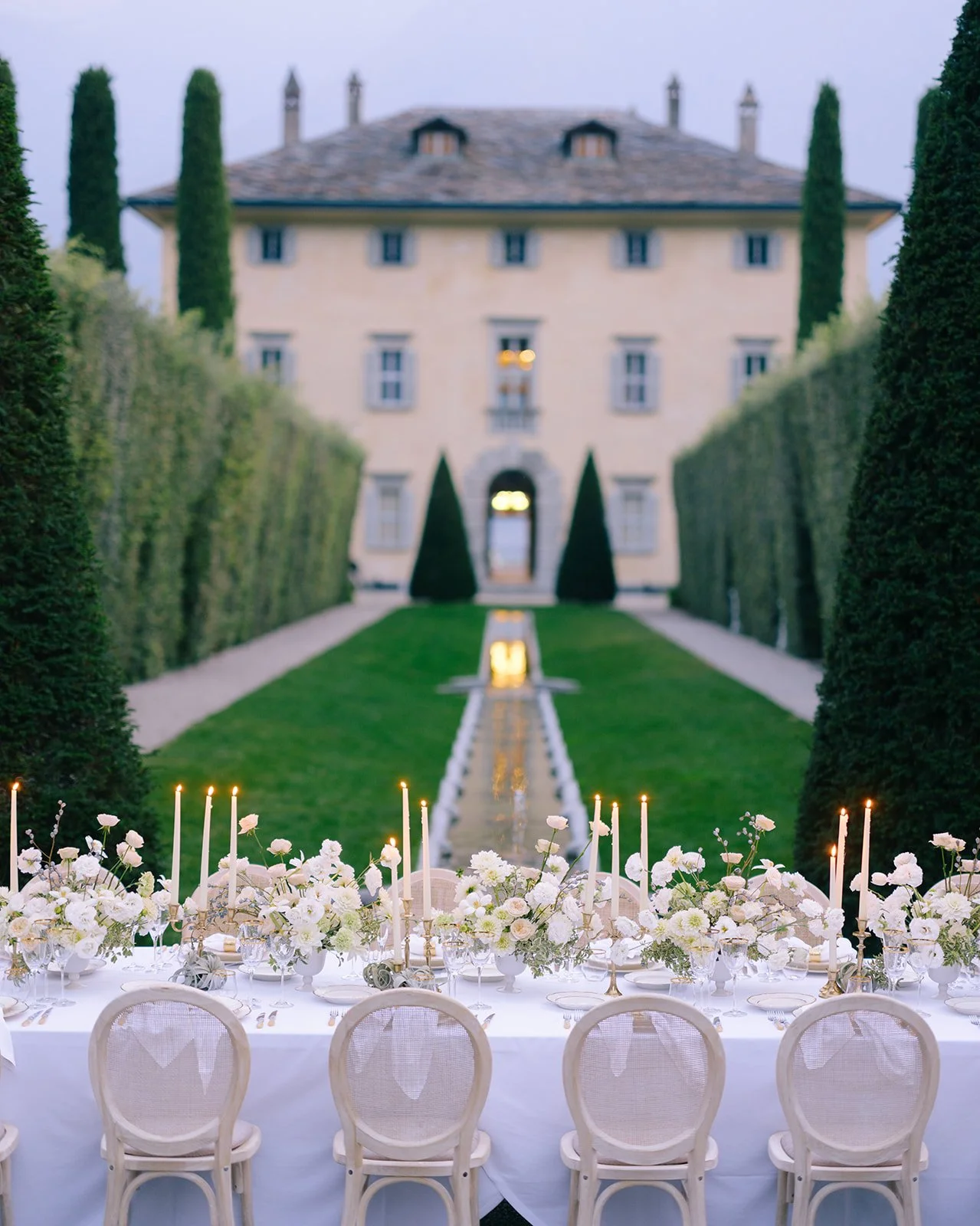 Long wedding reception table with white florals and candlelight in front of Villa Balbiano.