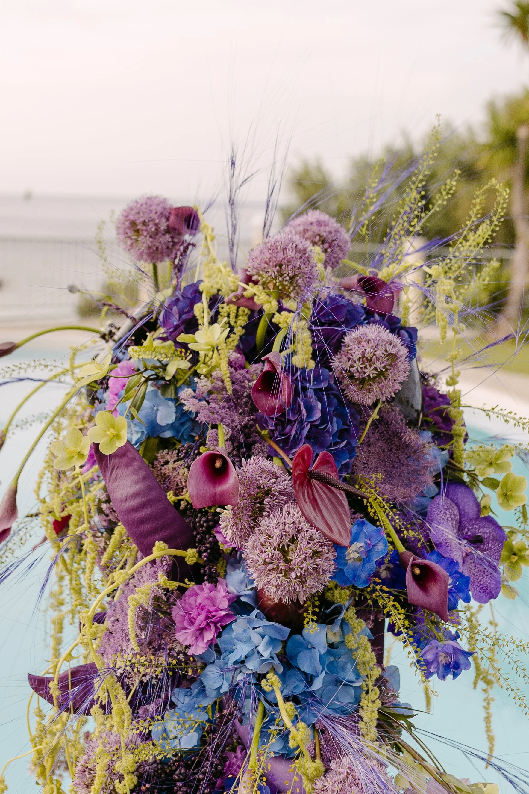 Tall sculptural floral installation in purple, blue and pink beside a private-estate pool in Crete.