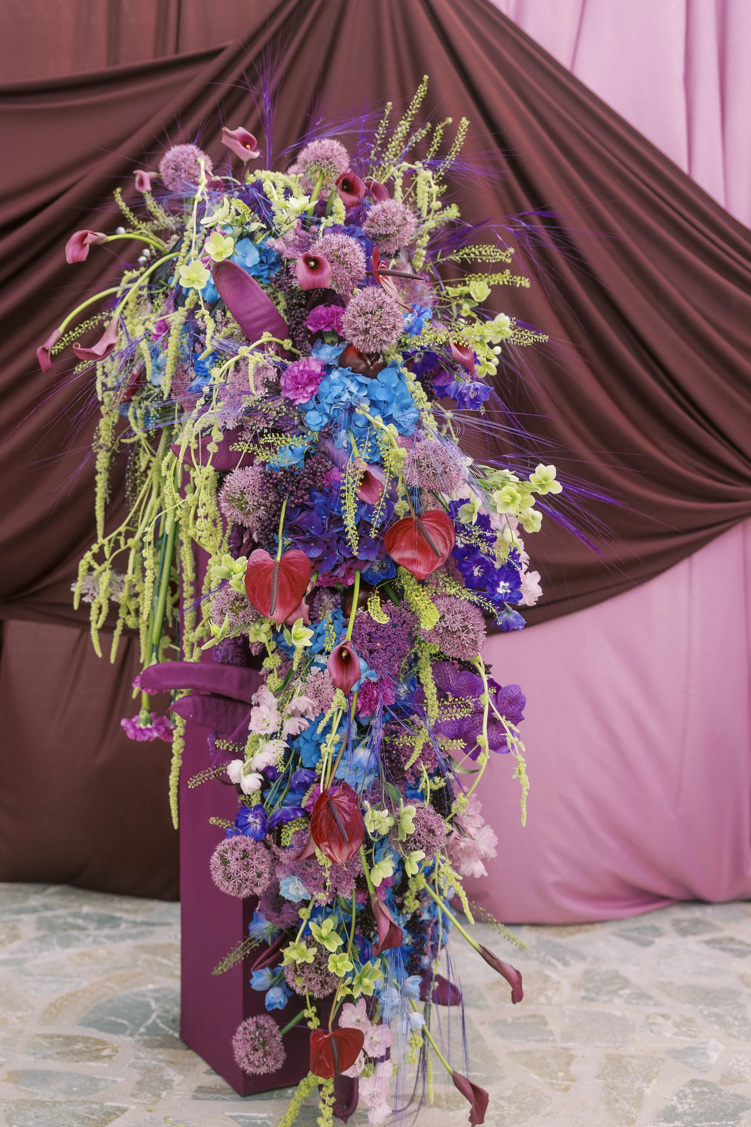 Statement purple and cobalt wedding flowers positioned against an aubergine ceremony backdrop.