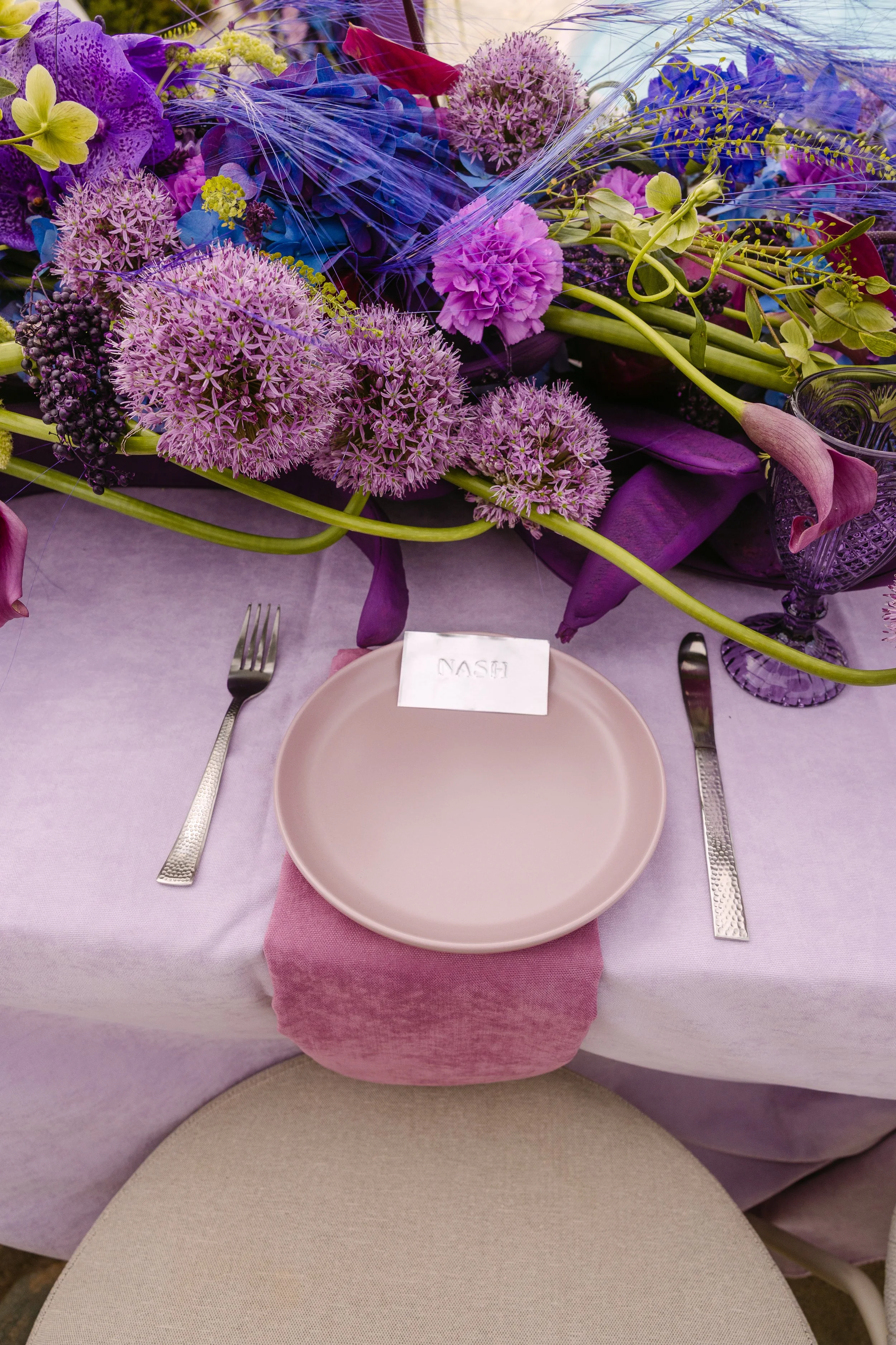 Contemporary wedding place setting with a mauve plate, dusty rose napkin and purple floral arrangement.