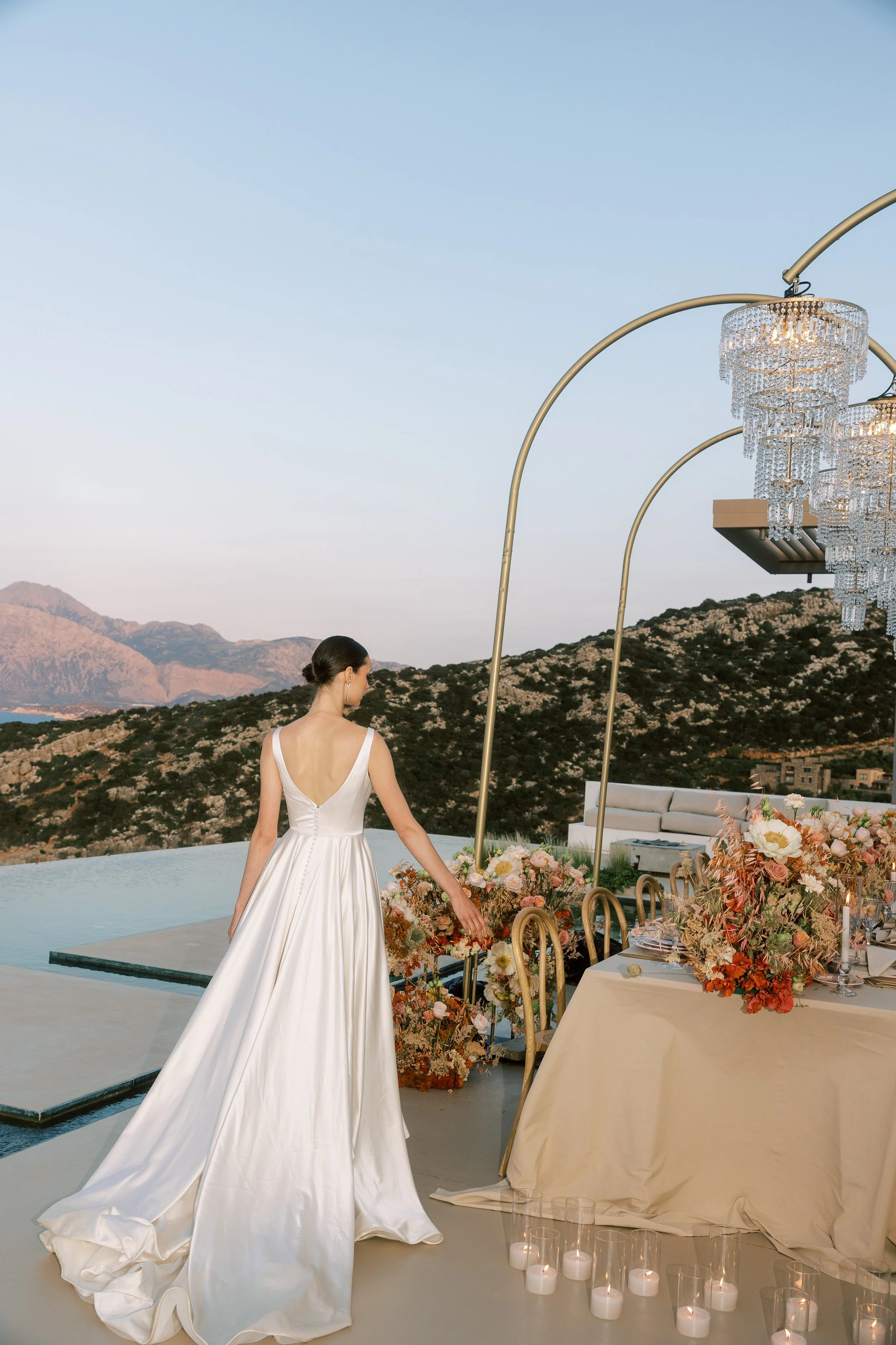 Bride walking beside an outdoor wedding dinner overlooking the Cretan landscape.
