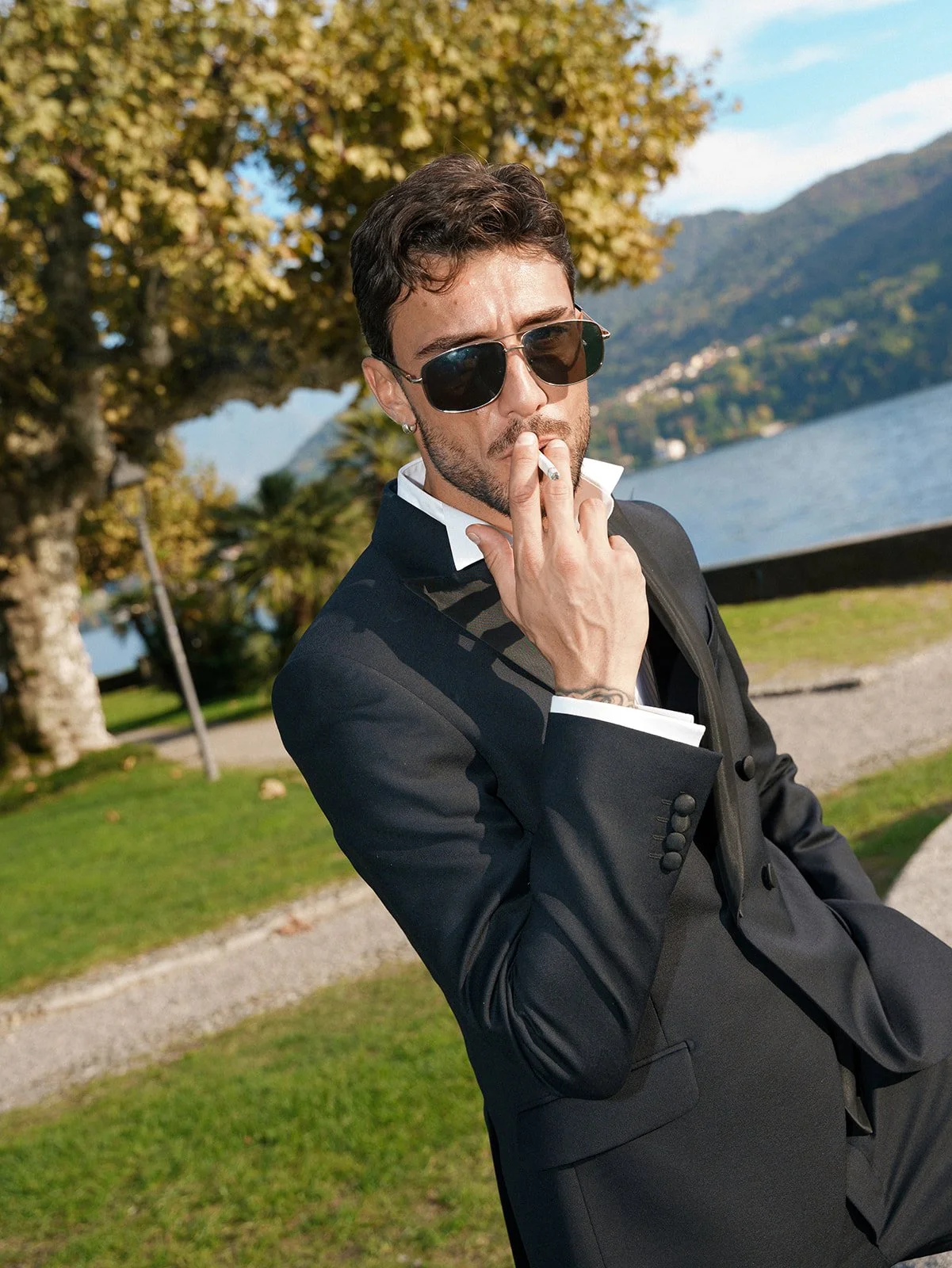 Groom in a black tuxedo and sunglasses standing in a historic lakeside garden on Lake Como.