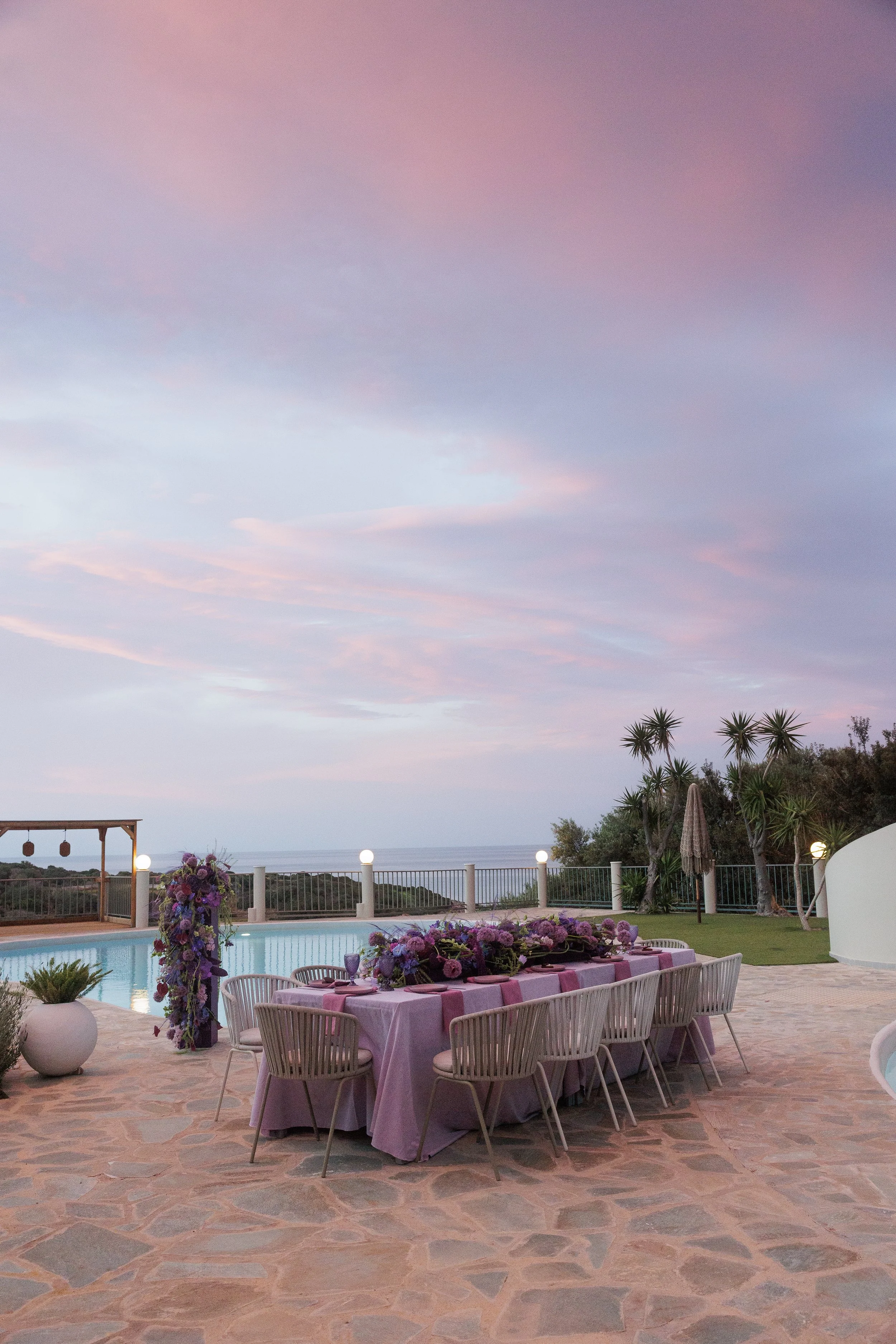 Colourful outdoor wedding reception in Crete with aubergine and lilac styling, sculptural purple florals and a sunset sky.