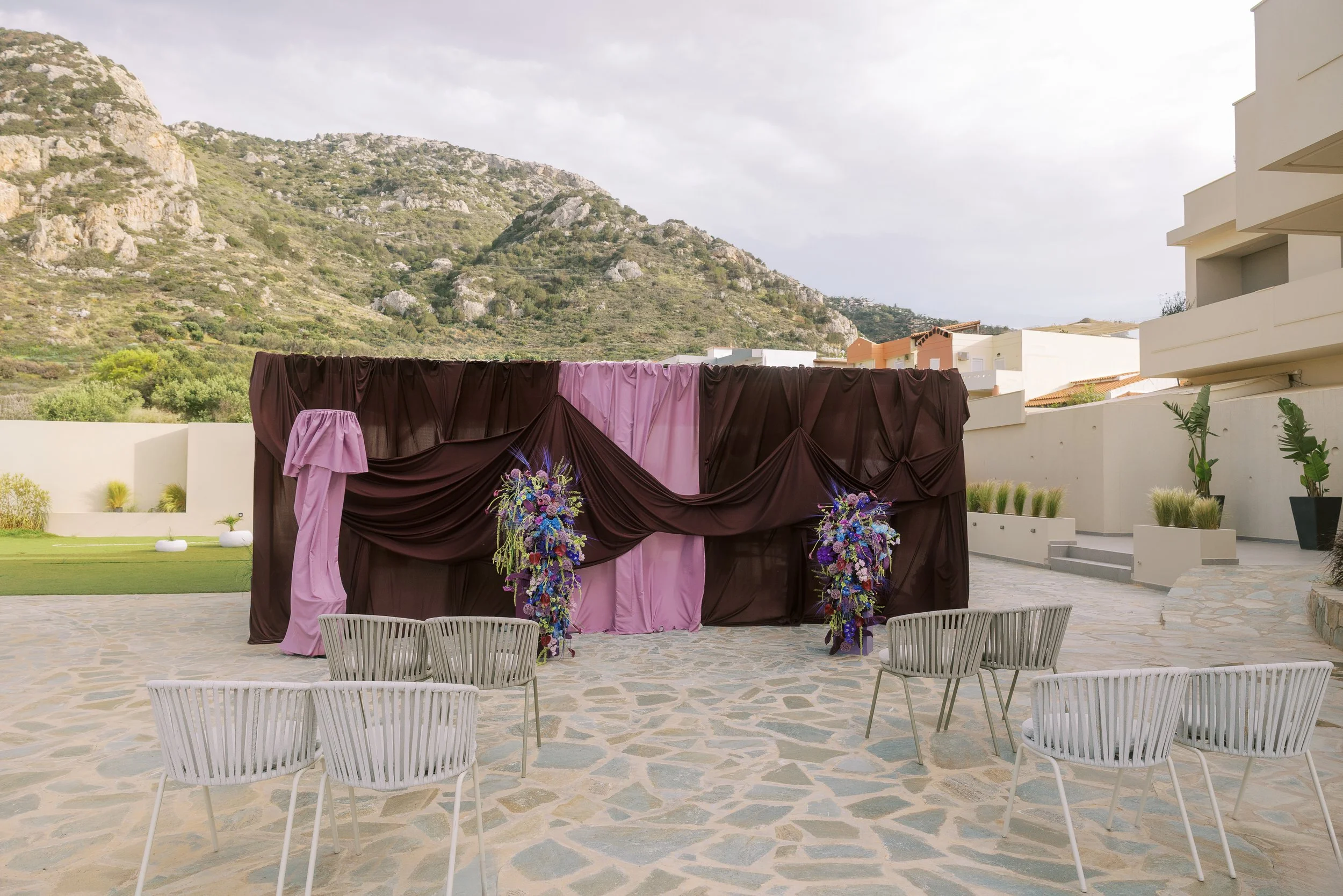 Wedding ceremony backdrop with brown and pink draped fabric and purple flowers in the hills