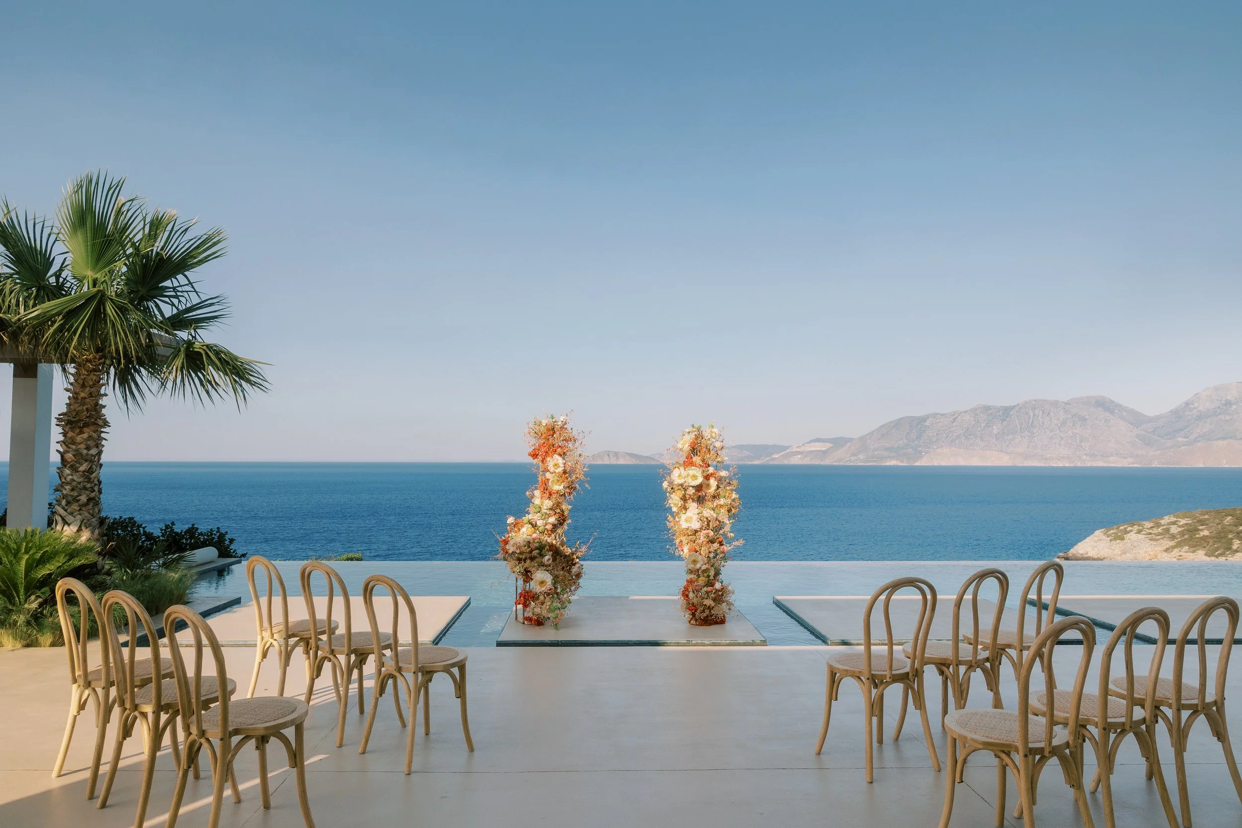 Open-air wedding ceremony with floral columns overlooking the sea at a private estate in Crete.