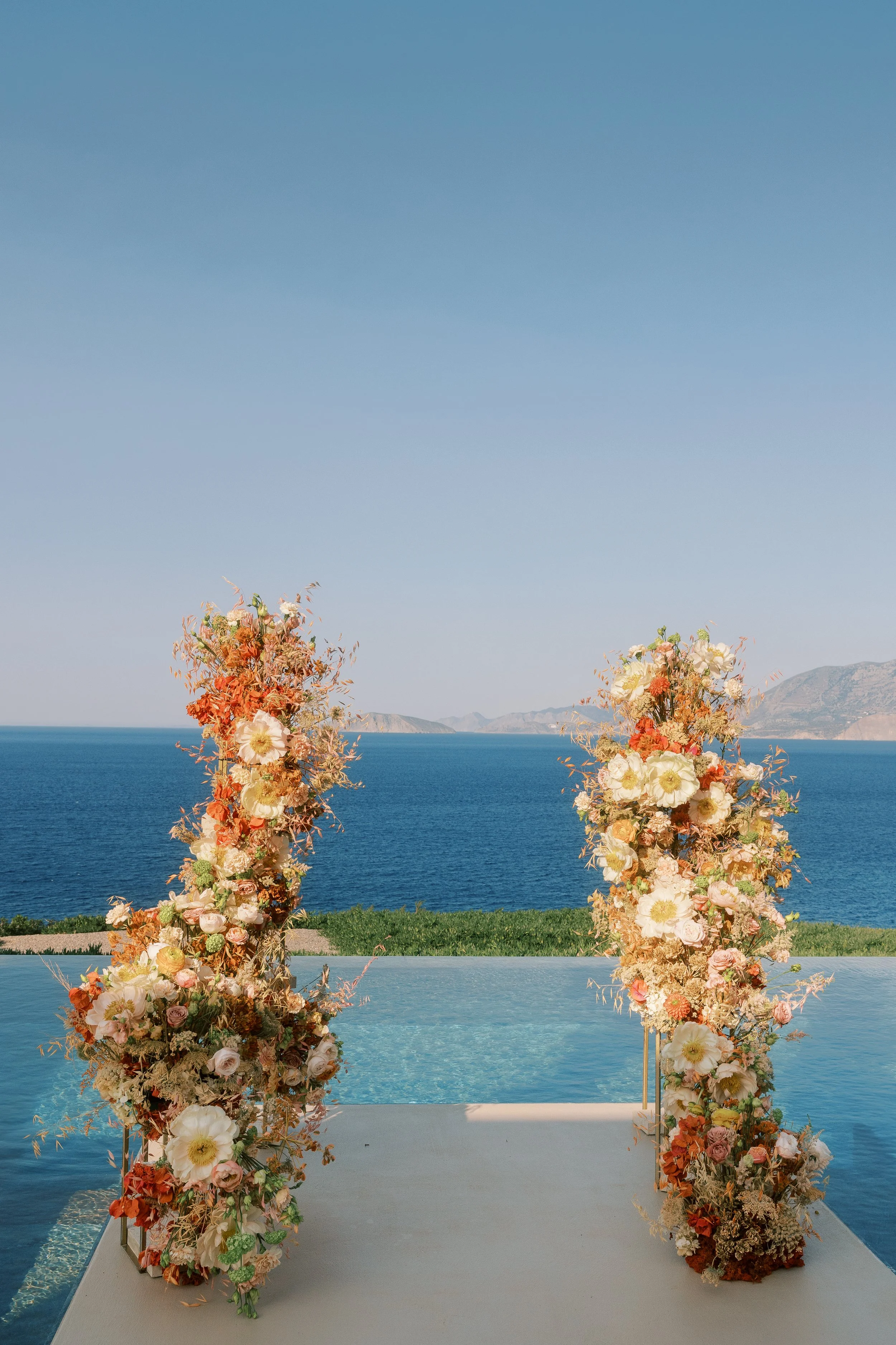Sculptural peach and ivory floral columns for a Mediterranean wedding ceremony in Crete.