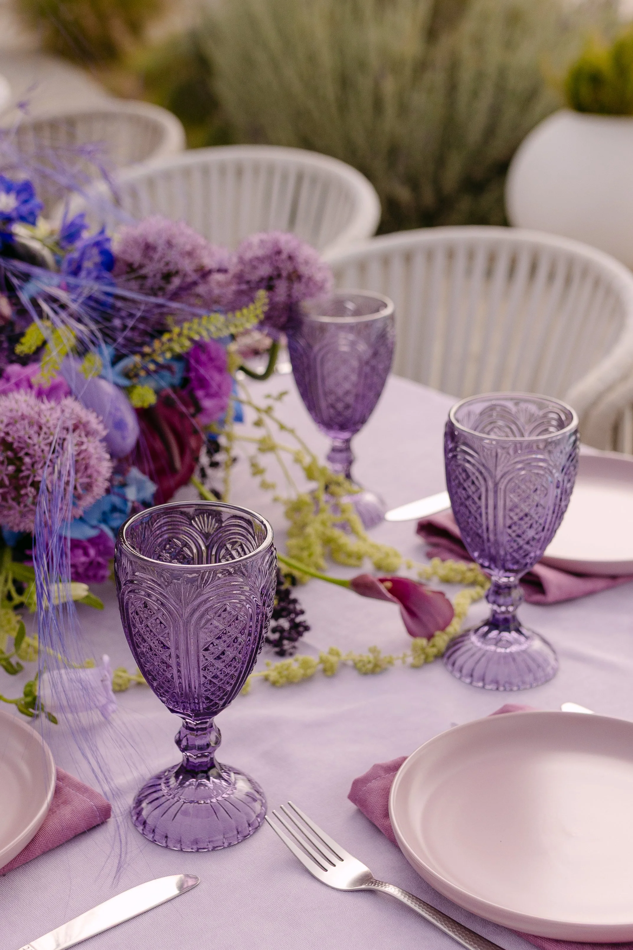 Smoky violet glassware and layered purple florals on a colourful wedding table in Crete.