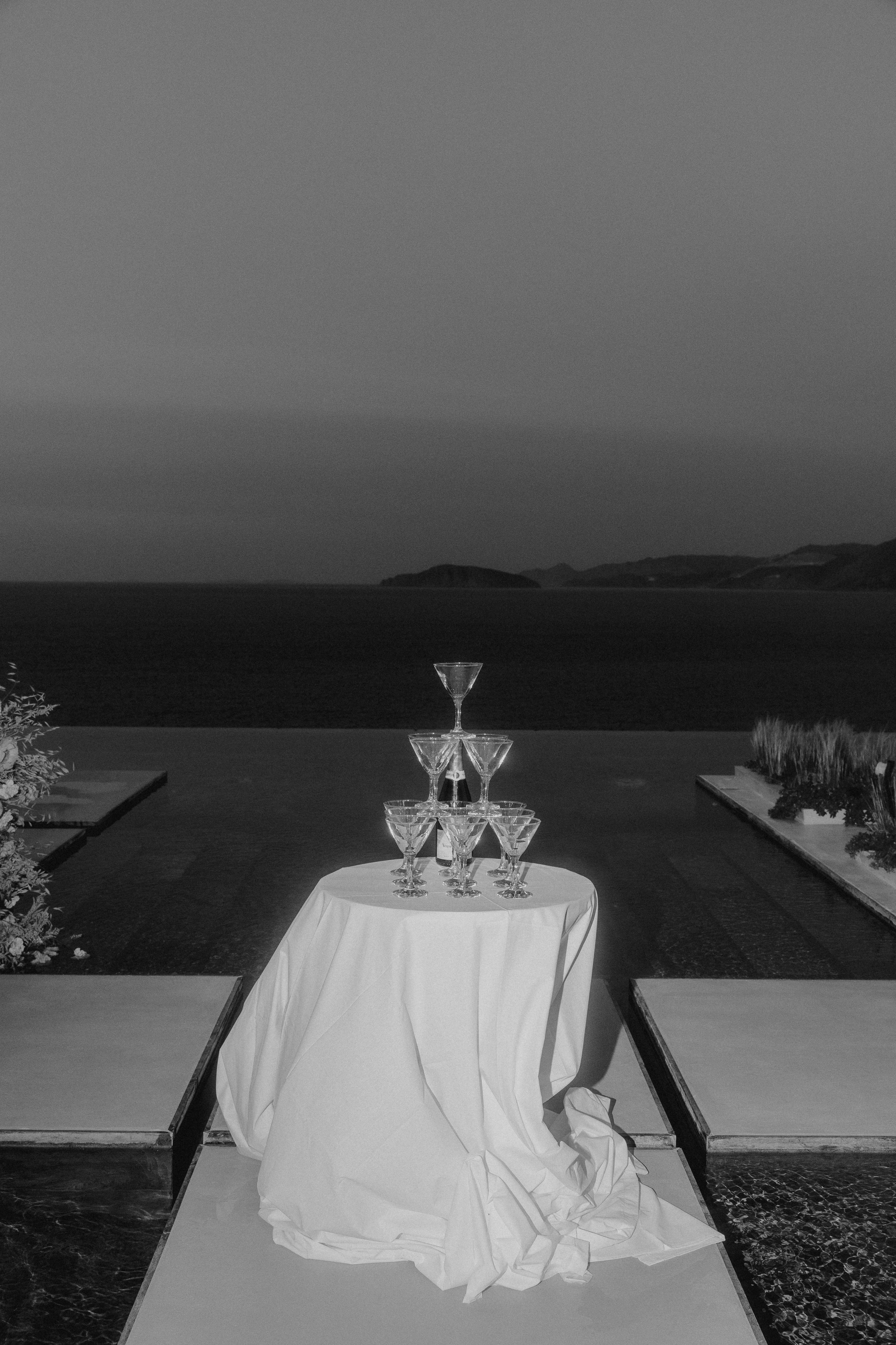Black-and-white view of a champagne tower overlooking the sea during an evening wedding in Crete.